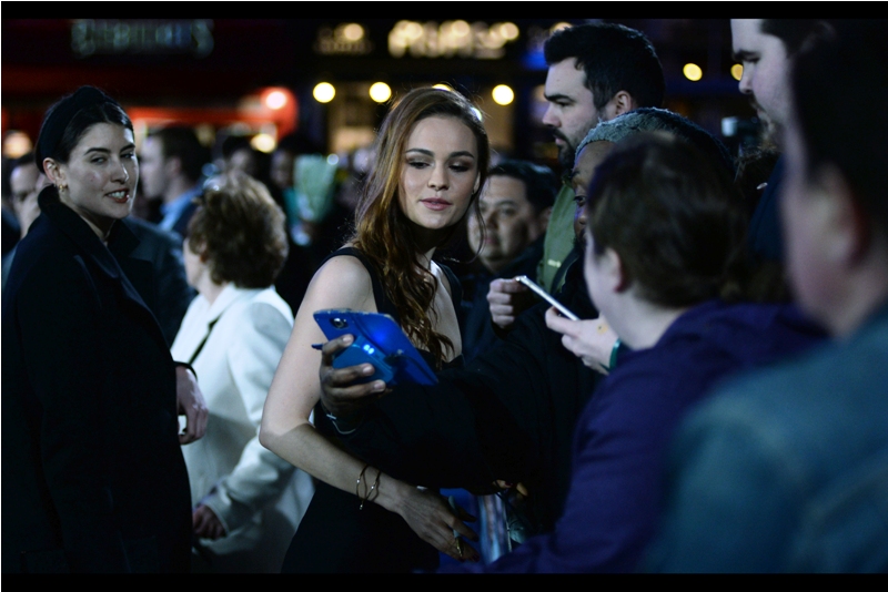 I don't know who this is (either), but she's prettier than the previous guy, and wearing less clothing than I am, and looking at that guy's holiday snaps like she genuinely cares. Now *that's* acting. (later edited to add : Sophie Skelton, and she's in this movie)