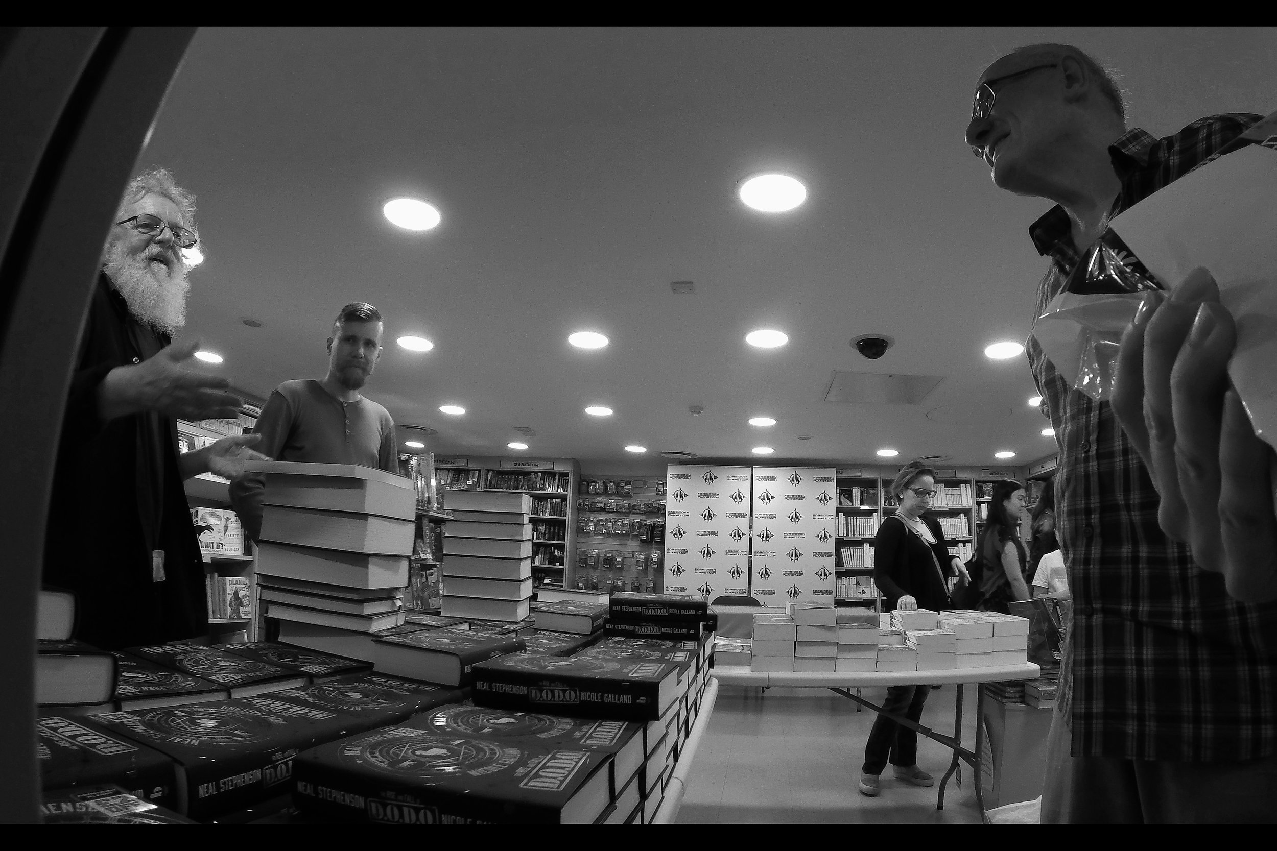 "who's the bigger fan of Neal Stephenson? Well, the guy on my left got here before me, but I think you'll find my pile of books to be signed is higher. I notice you bought a single book to be signed... that's so sweet"