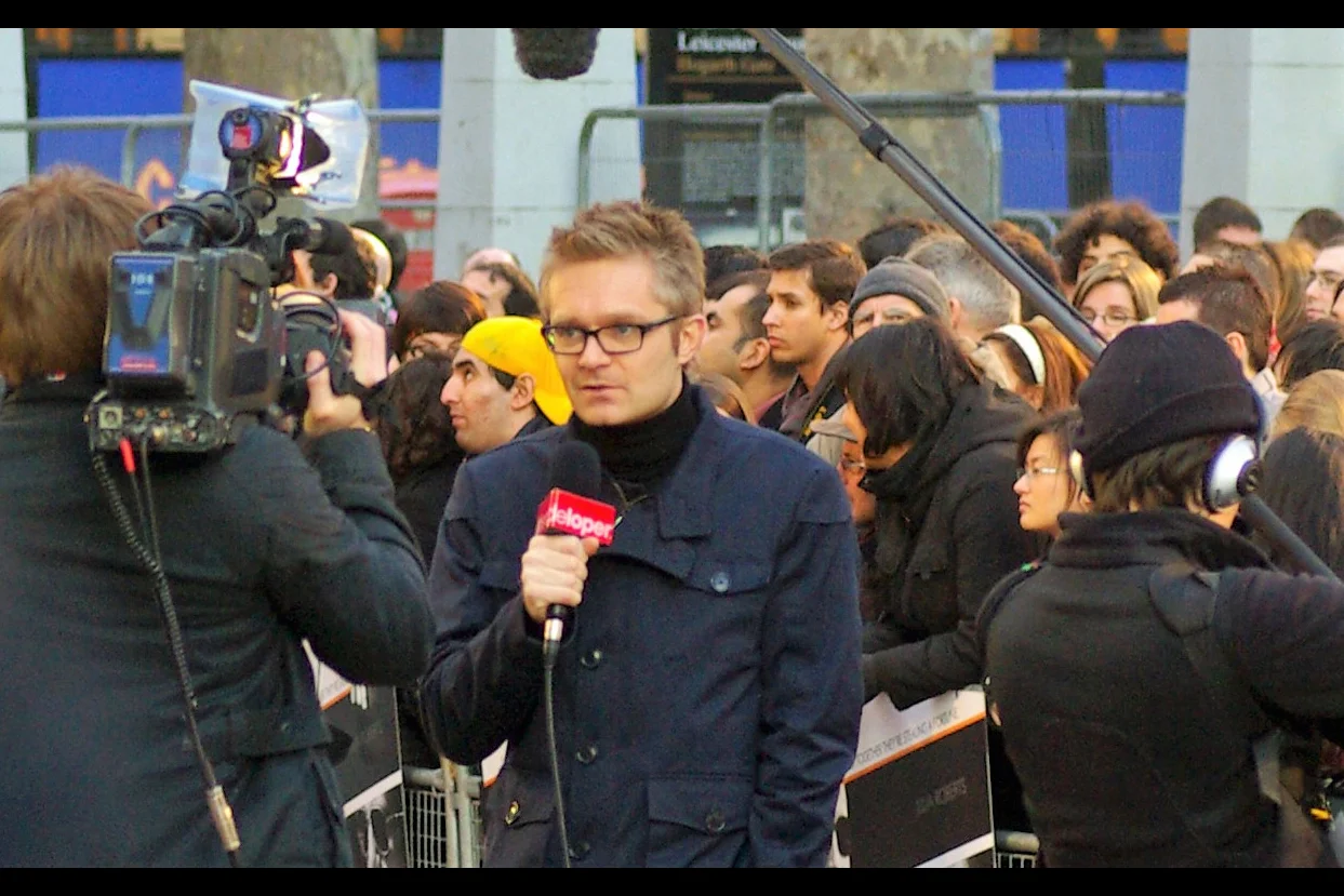 "Tom, I'm standing here in Leicester Square for tonight's premiere. Julia Roberts may attend. Clive Owen may attend. The dude with the Pentax is almost certainly going to be here. But everyone's wondering : Where is Yellow Cap Guy?"