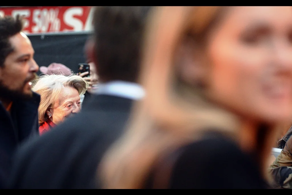 A massively raucous squeal and cheer rises from the crowd as Dame Maggie Smith (aka “Violet Crawley, Dowager Countess of Grantham”) rushes past fans and zips into the cinema, declining to be interviewed on stage, and using the crowd as cover and security as a buffer zone. This is one of three shots I took of her, and this was the second best. I punished my butler for the failure.