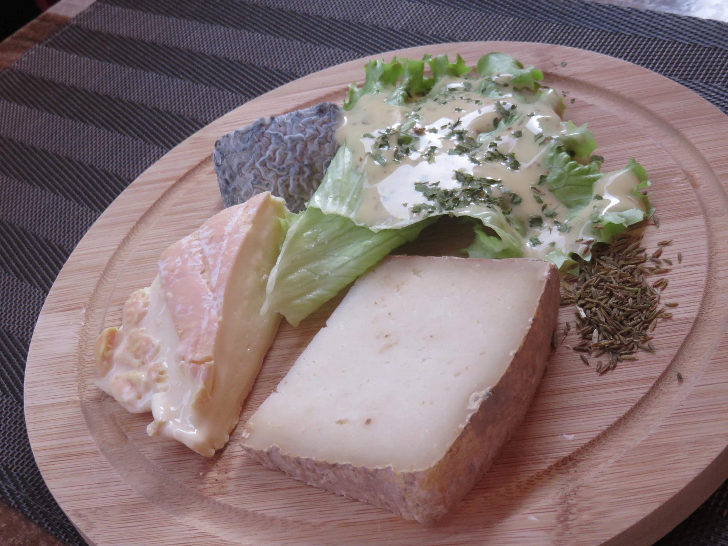 Dans le sense des aiguilles de l'horloge à partir de la salade : les graines de cumin (pour accompagner le munster), le tomme d'Alsace, le munster, et le chèvre cendré.