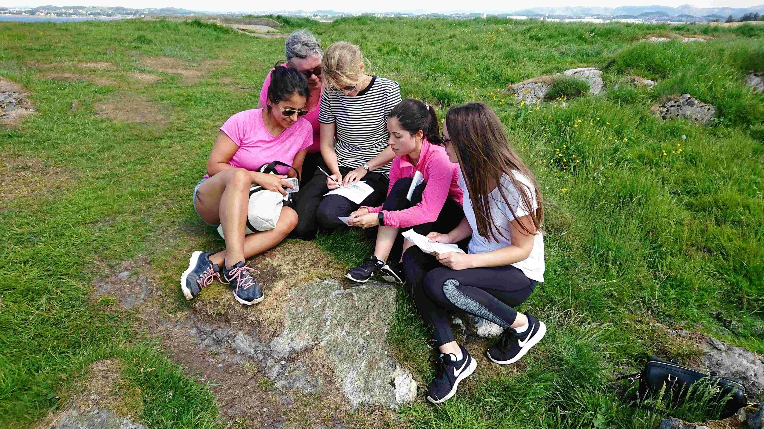 Smilende kollegaer sitter på gresset og samarbeider om oppgaver under mysterievandringen Operasjon Fortitude.