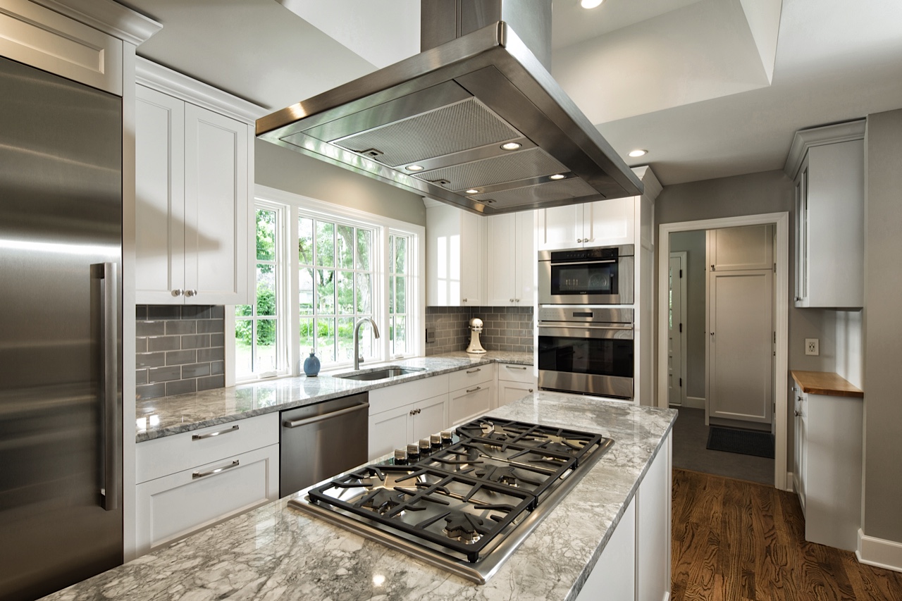 After: Cooktop integrated with usable workspace and ventilation on the island. Multiple ovens stacked in an integrated cabinet column. Easy triangle flow from sink to cooktop to ovens, with room for a mixer and a dough slab in between.