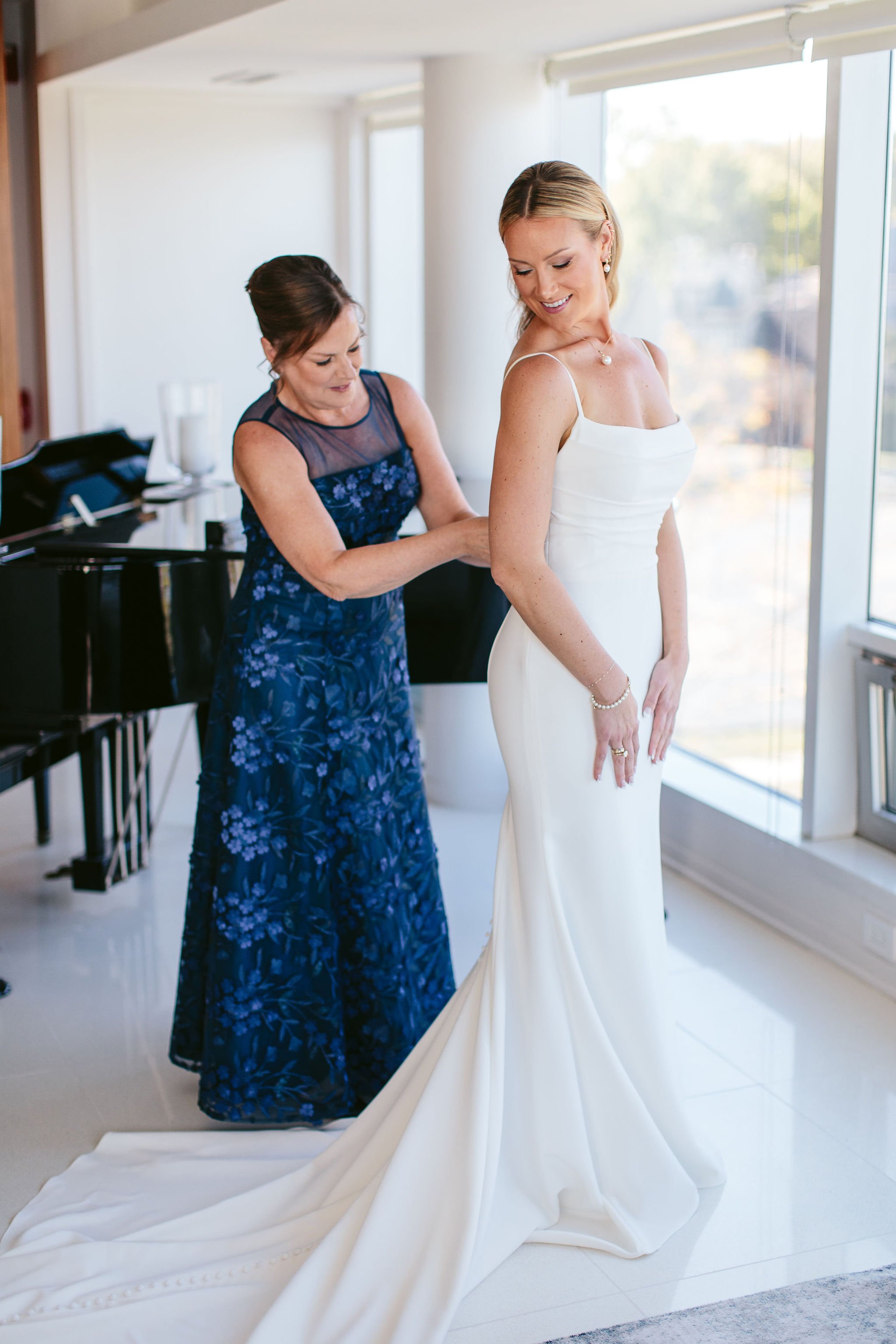 mother of the bride helping daughter put on wedding dress