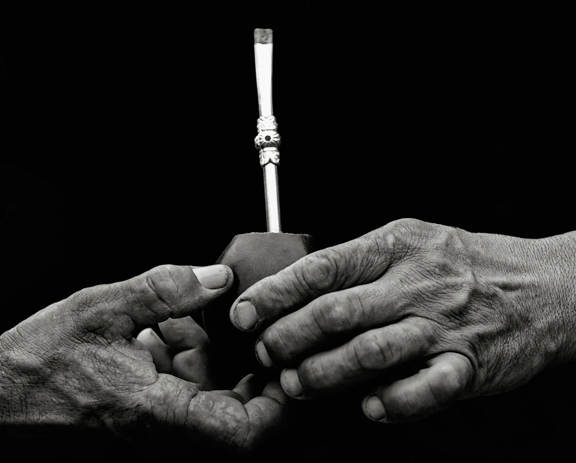 Veiny, weathered hands of a working man holding a mate gourd and a silver straw