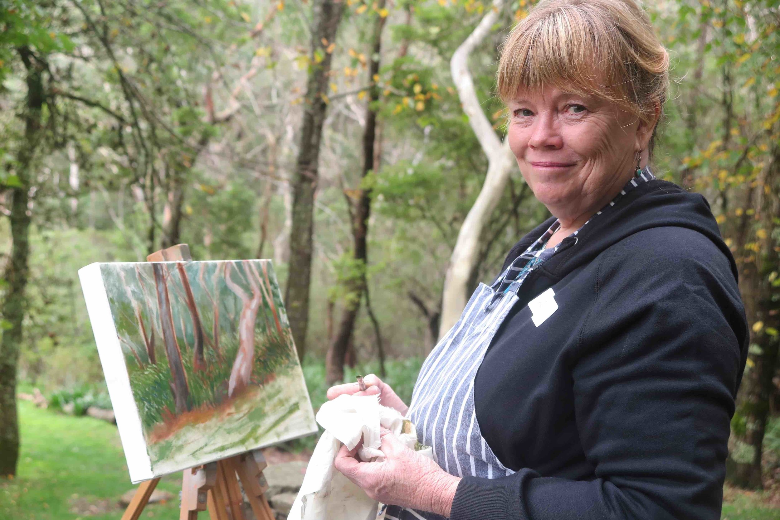 small Winmalee resident, Sue with her 'in progress' oil painting of the bush beyond the garden.jpg