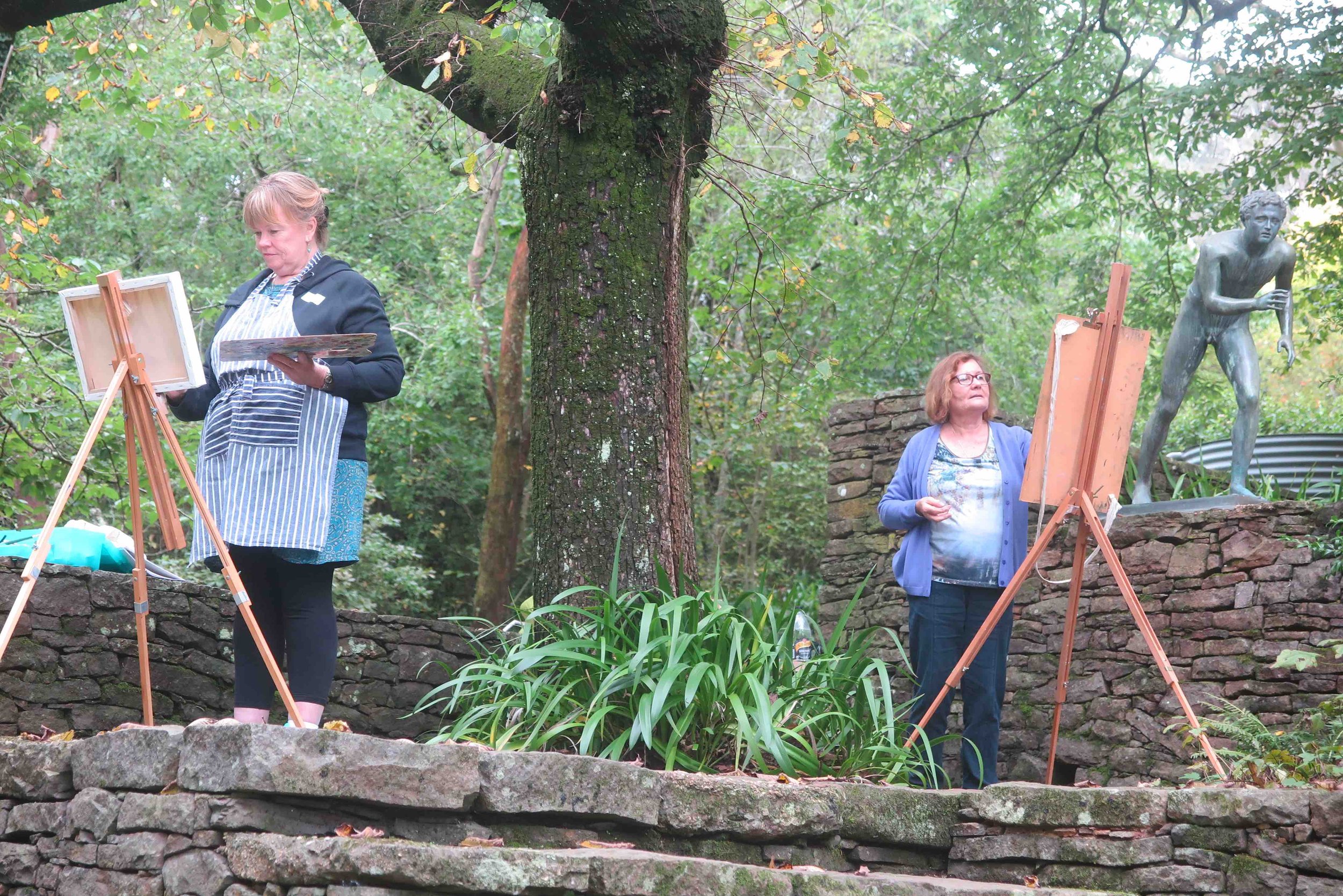 Two painting retreat participants working at easels with garden scenery around them