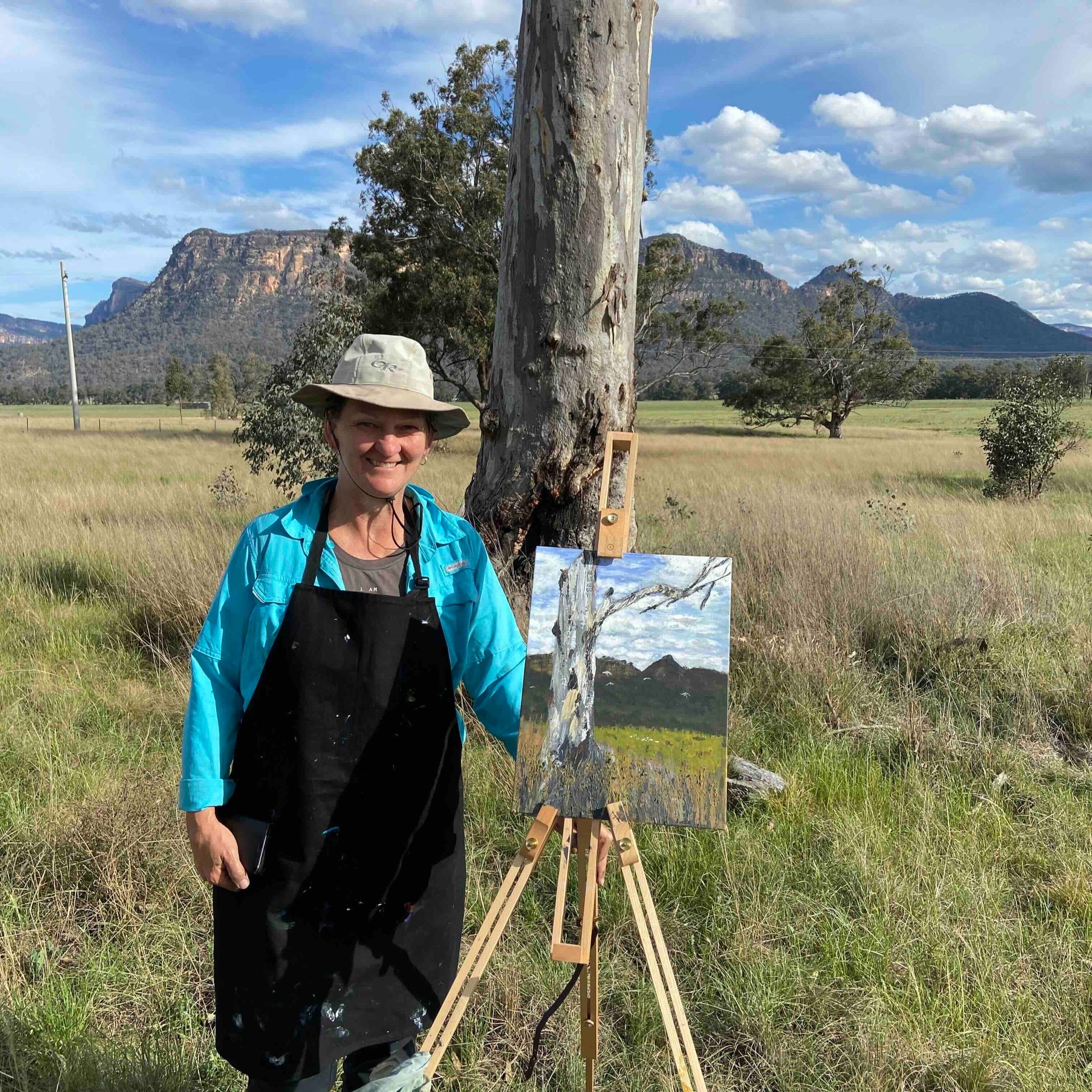 Retreat attendee with her landscape painting of a tree, Caoertee mountains and the paddocks