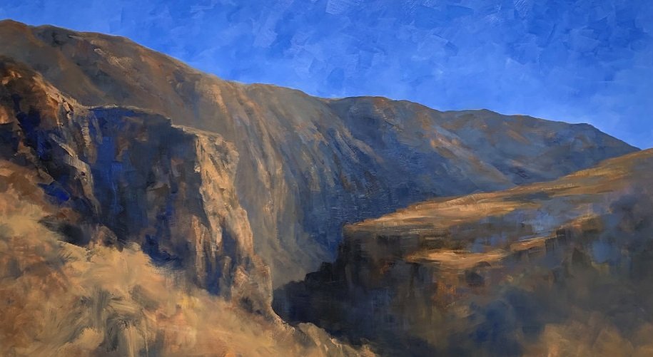 A large rectangular painting of desert mountains in red ochre with blue sky behind