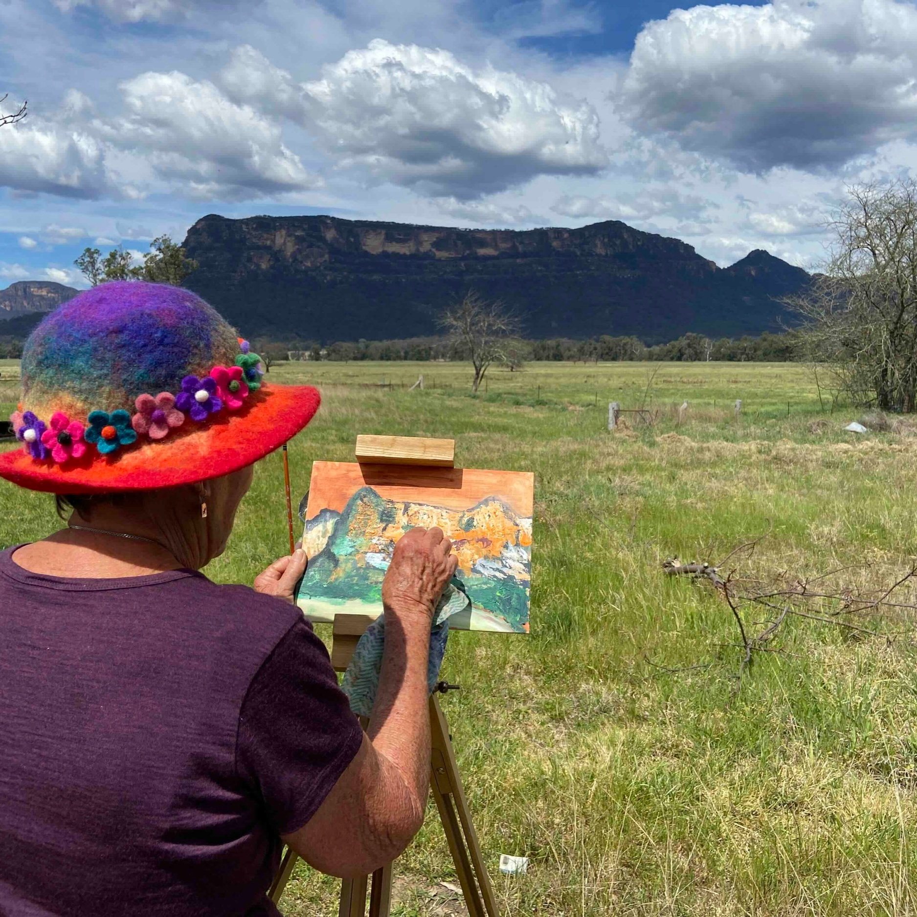 A plein air painter on retreat in the Capertee Valley, working on her painting with brightly coloured hat on