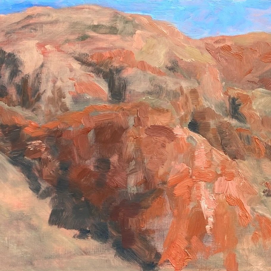 Orange mountain range in desert plein air painting with blue sky behind