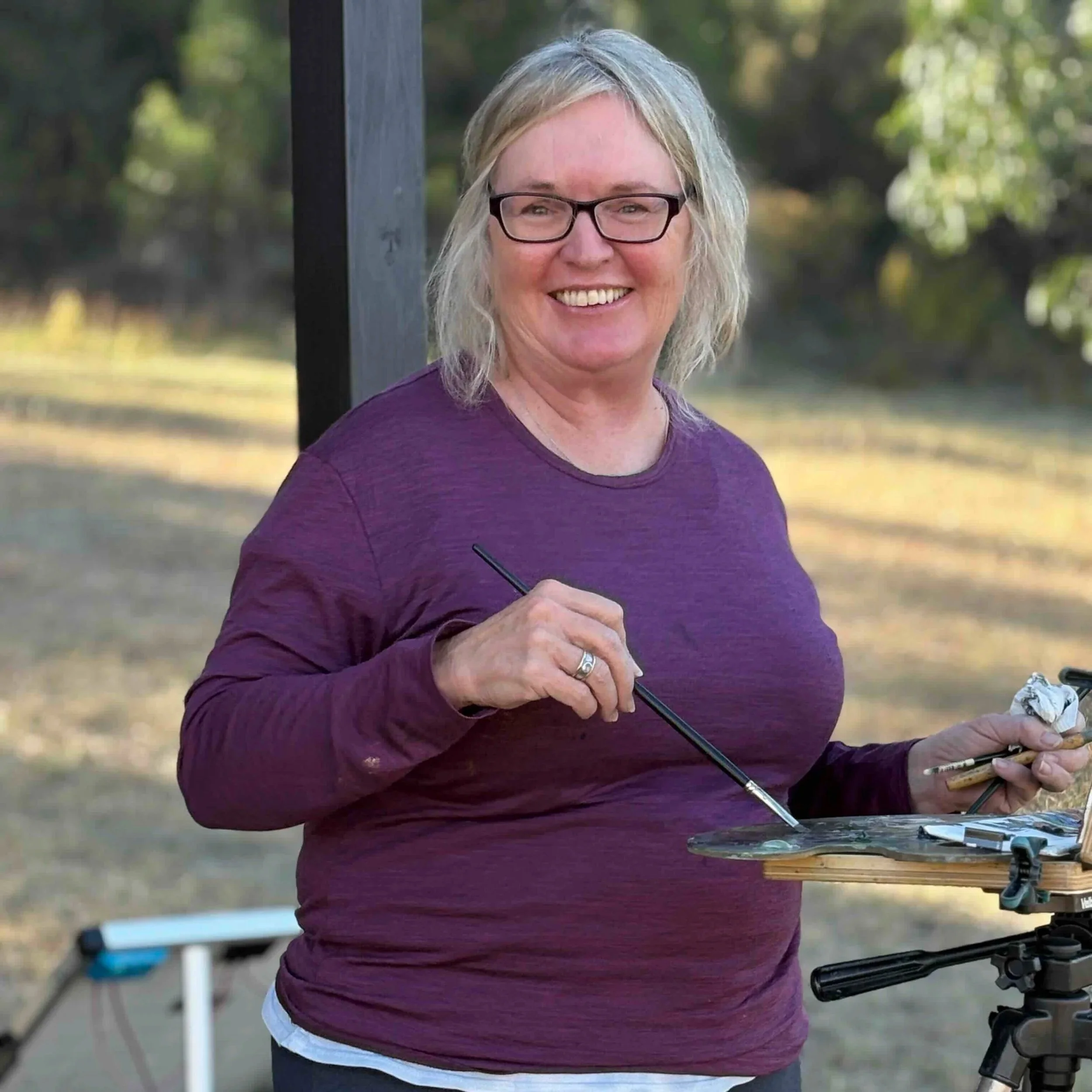 Female artist smiling at her painting on easel in Capertee Valley 