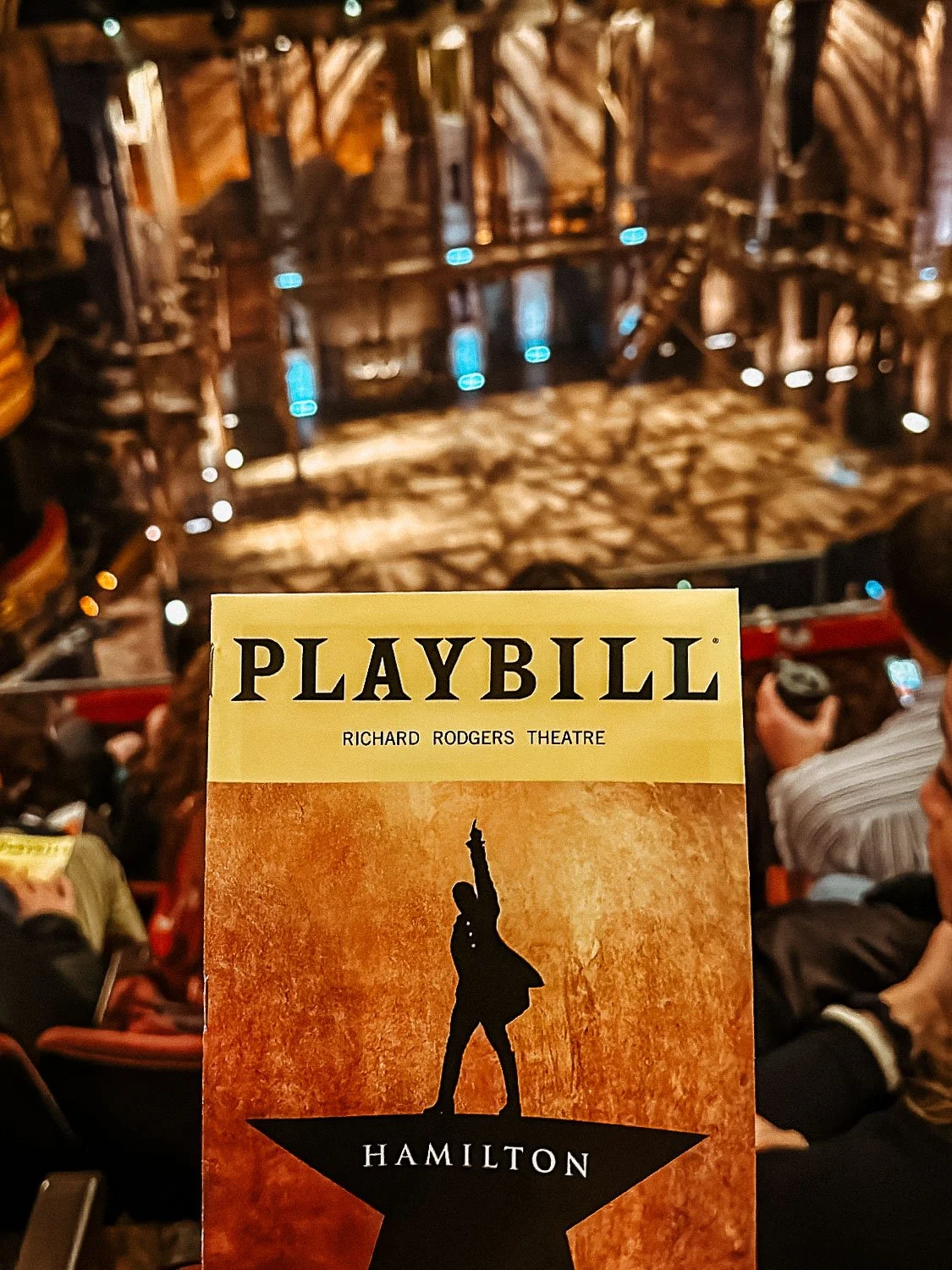 The Broadway Show Hamilton stage is the background with the playbill up front and center.