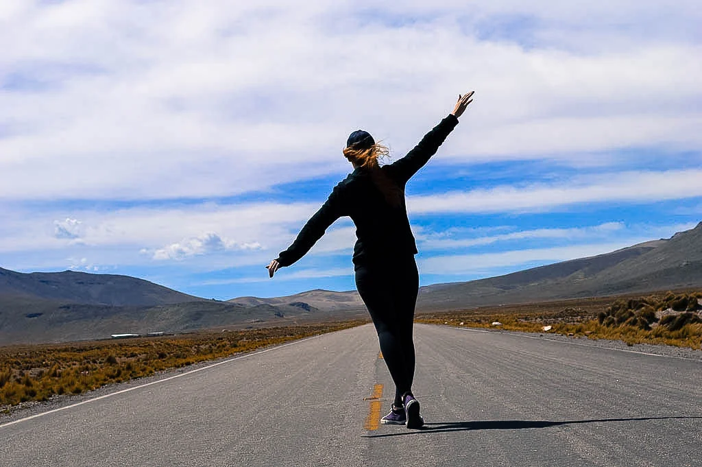 A redheaded woman wearing all black standing in the middle of the road in the Salinas and Aguada Blanca National Reservation in Arequipa Peru.