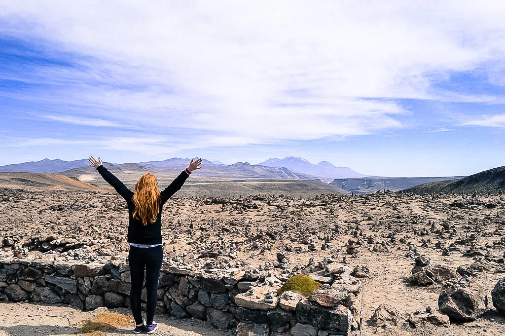 A redhead female traveler looking out to the Mirador de Los Andes starting at stacked rocks at the top of a mountain.