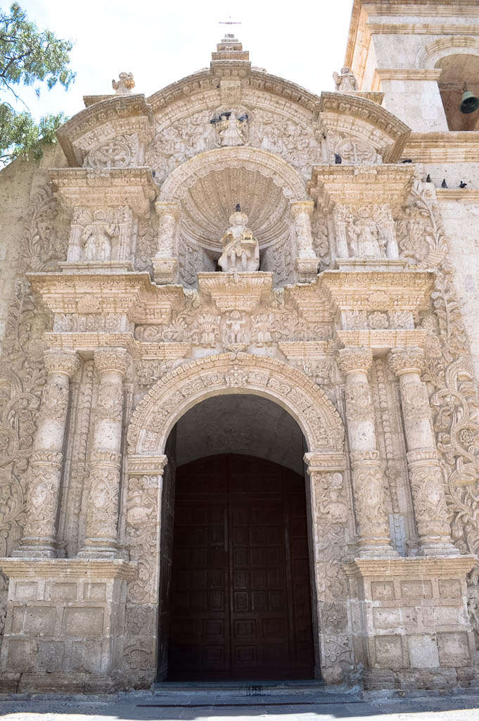 The door entry to San juan Bautista Church Yanahuara Church in Arequipa Peru. There is a wooden door with white sillar carved rock, carved white pillars and white architecture.