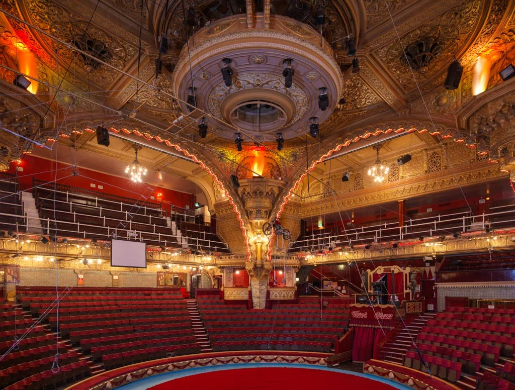 The inside of the Blackpool Tower Circus theatre, with golden archways, red velvet seats, and a bicycle suspended in the air.
