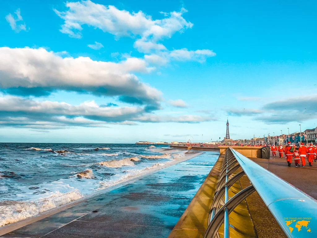 View of the Blackpool tower and promenade on the Santa Dash with people running in Santa Claus outfits.