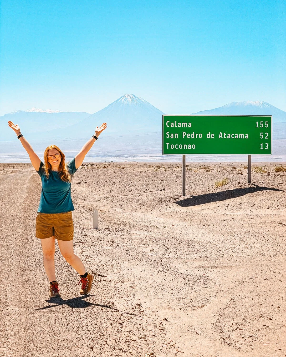 Highway sign showing distances to Calama, San Pedro de Atacama and Toconao with volcanoes behind, Atacama Desert Chile