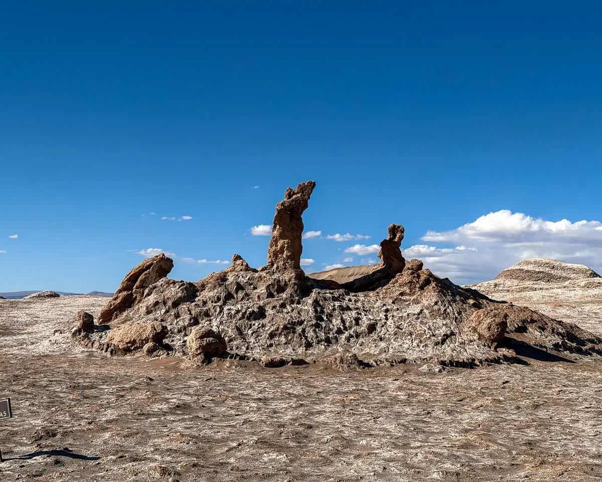 The tres marias rock formation, three rocks sticking up from the landscape. The ground is brown and white in color due to the salt, and a clear blue sky in the valle de la luna in atacama desert chile