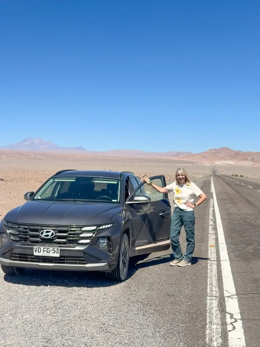 Grey rental SUV parked on an empty desert highway with a volcano in the distance, on the self-drive route in the Atacama Desert, Chile