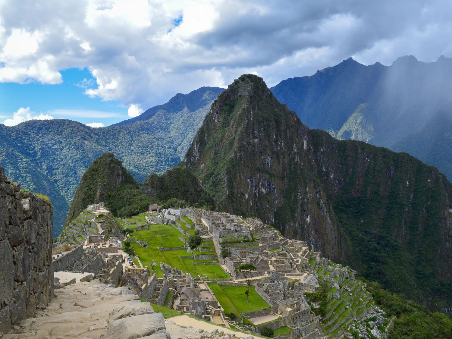 A view of Machu Picchu in Peru. It is a sunny day and there are mountains and the citadel visible.