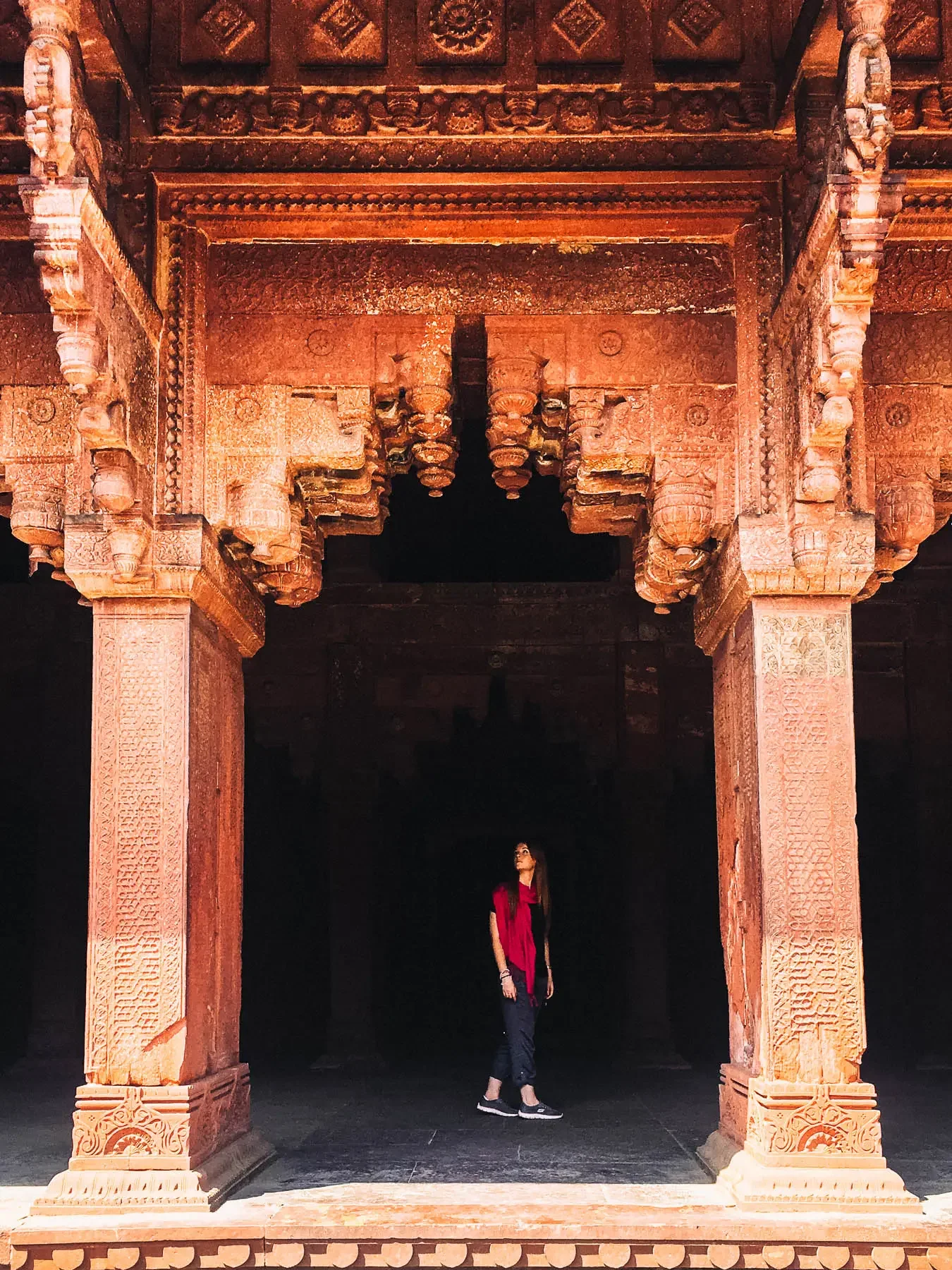 A woman looking up at the arch way of a detailed decorative arch in Agra Fort, India.