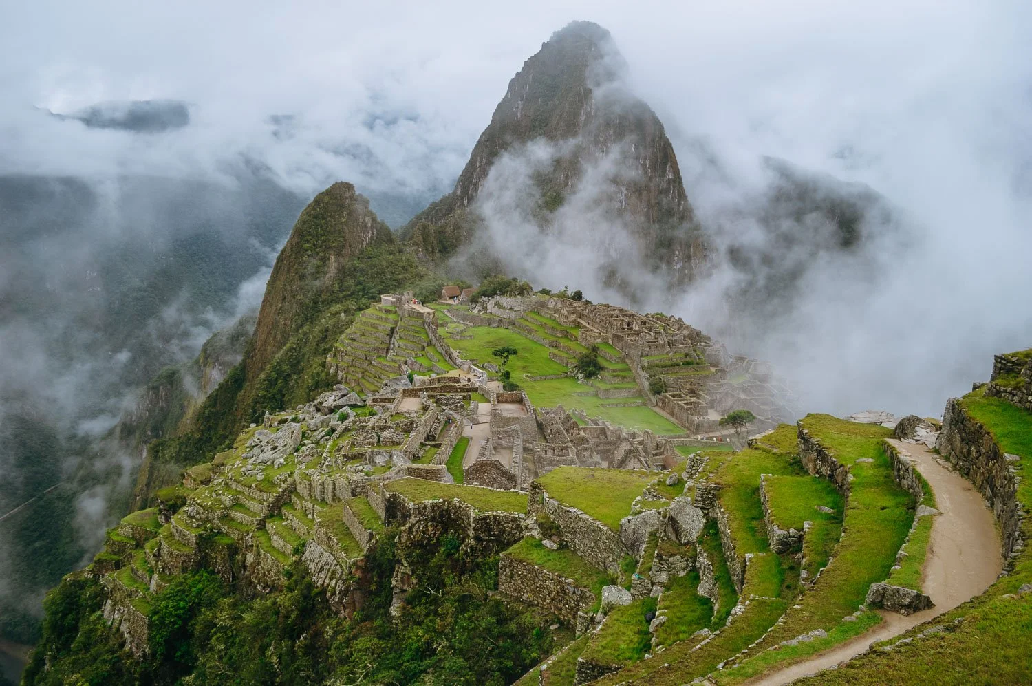 Viewpoint of Machu Picchu where mist rain and clouds are covering some of the site.