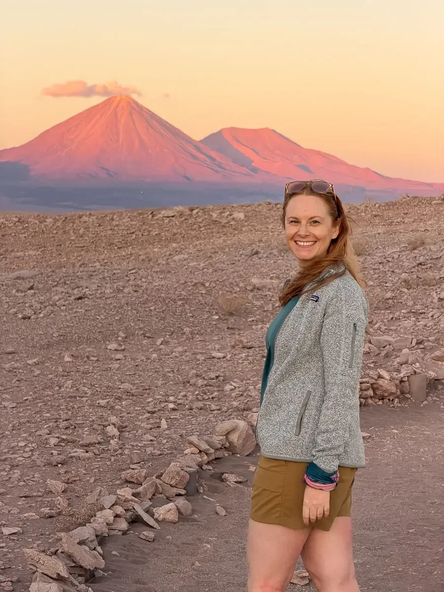 A redheaded girl in hiking clothes in front of the volcano visible from valle de la luna at sunset in the atacama desert in chile