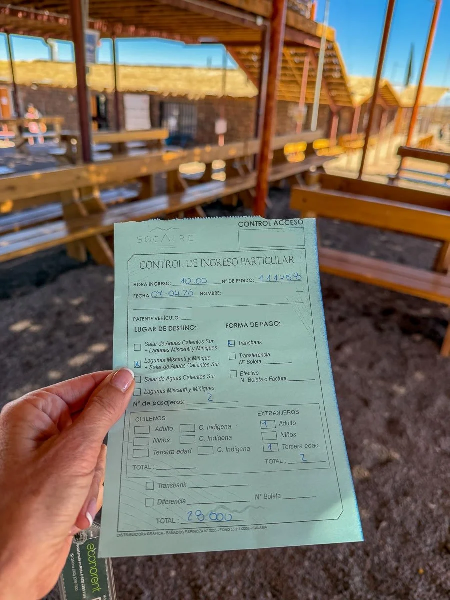 Hand holding a paper entry permit issued at the Socaire check-in office for Lagunas Miscanti, Miñiques and Piedras Rojas, Chile