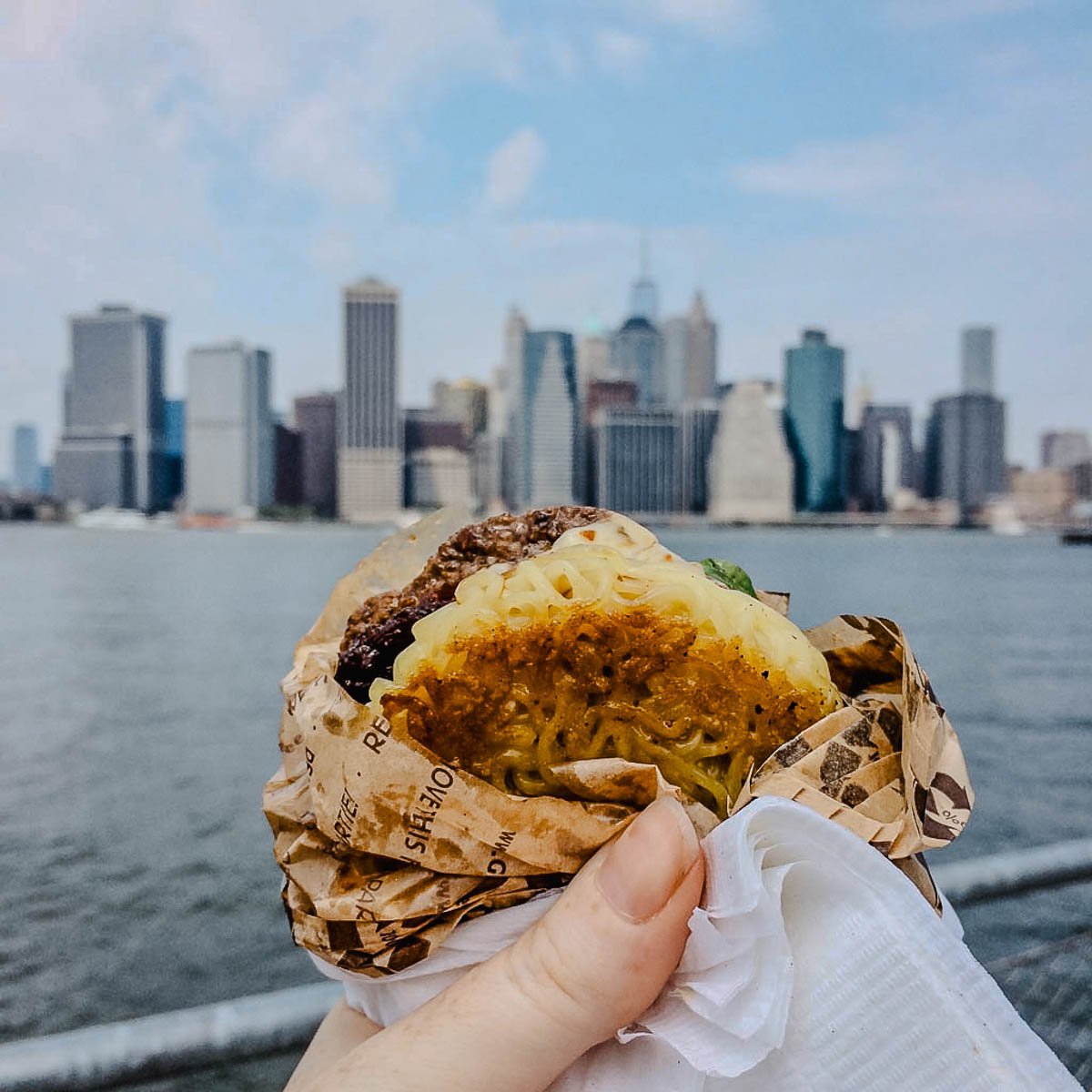 a ramen noodle burger raised up in front of the nyc skyline