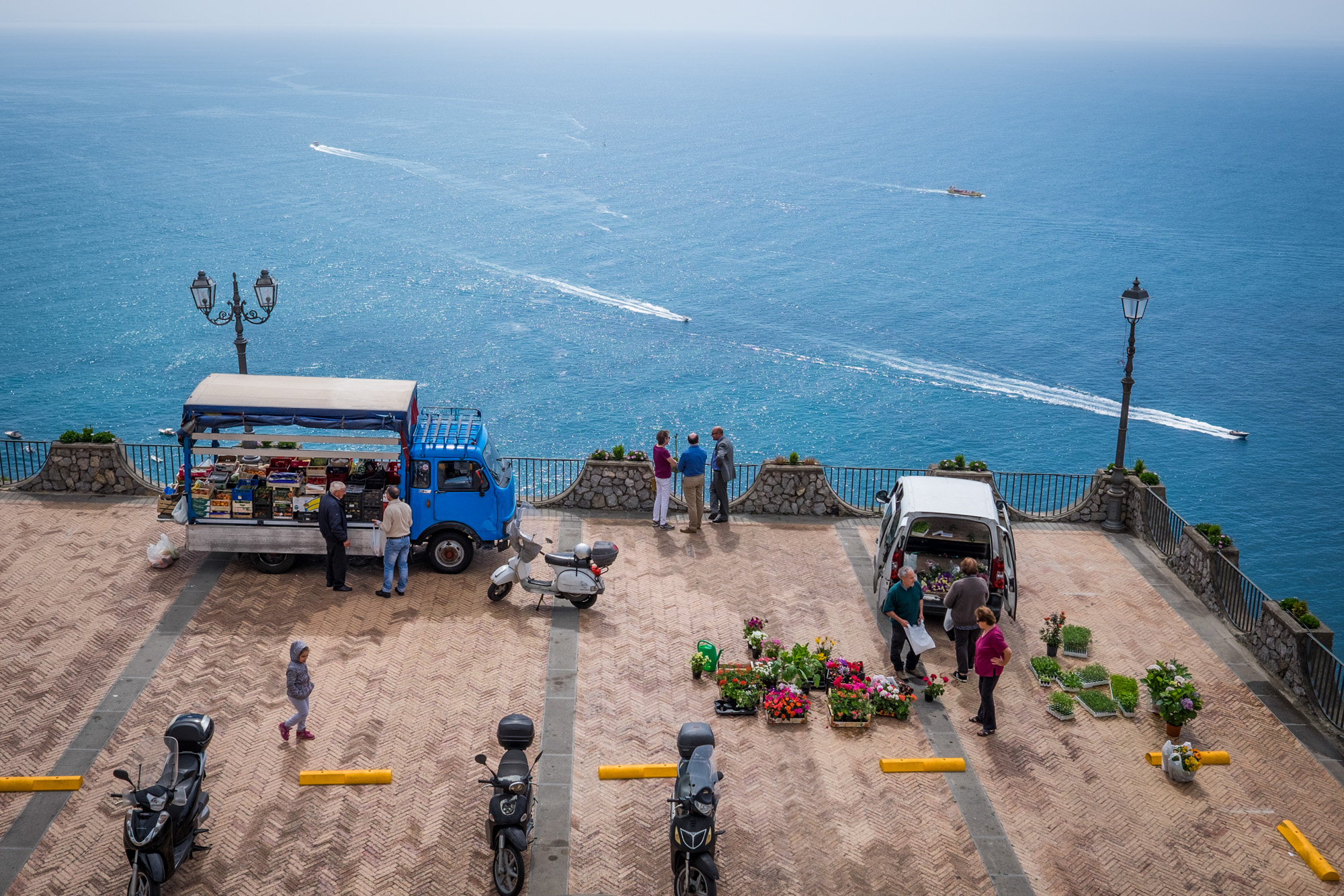 ITALY, Praiano: People gather at a market as boats sail past in the Mediterranean Sea.