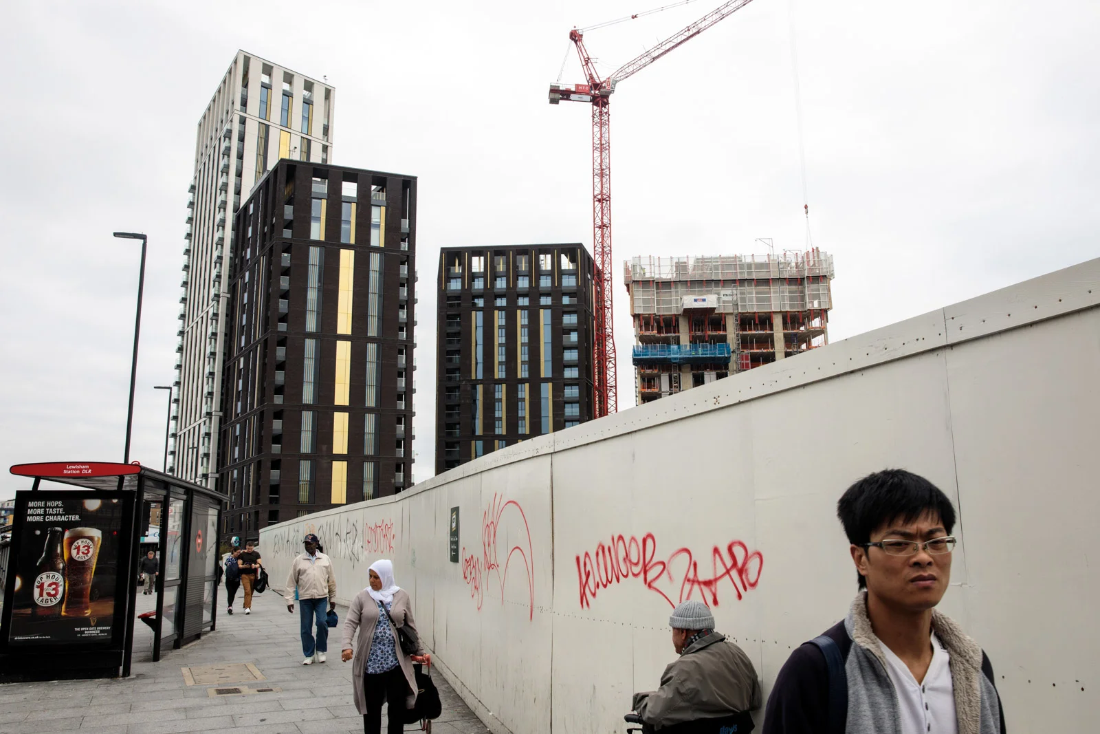 Cranes tower over a building development underway as people walk past a bus stop in Lewisham on August 22, 2017 in London.
