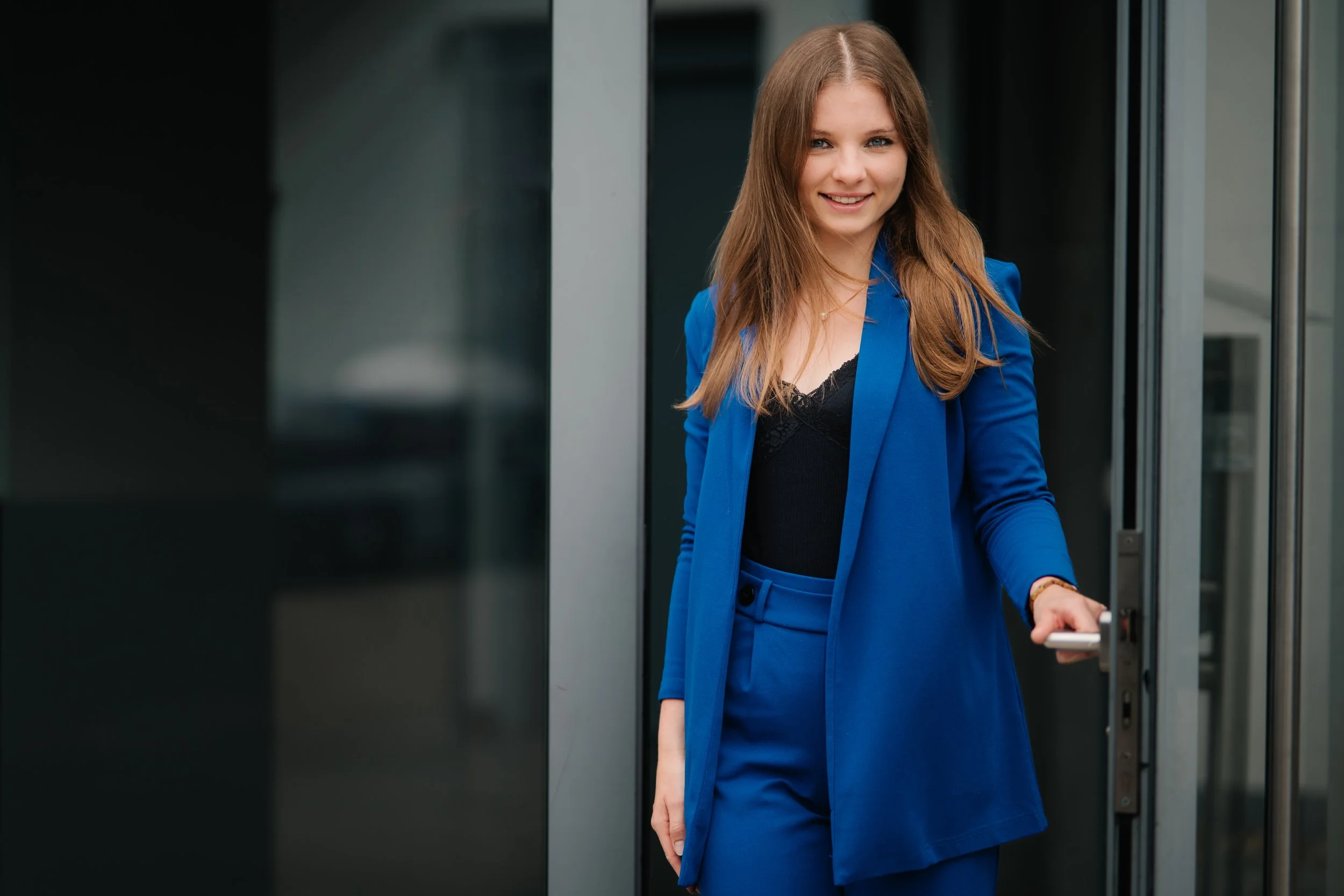 Eine junge Frau mit brünetten Haaren in einem blauen Anzug, die eine Tür öffnet.