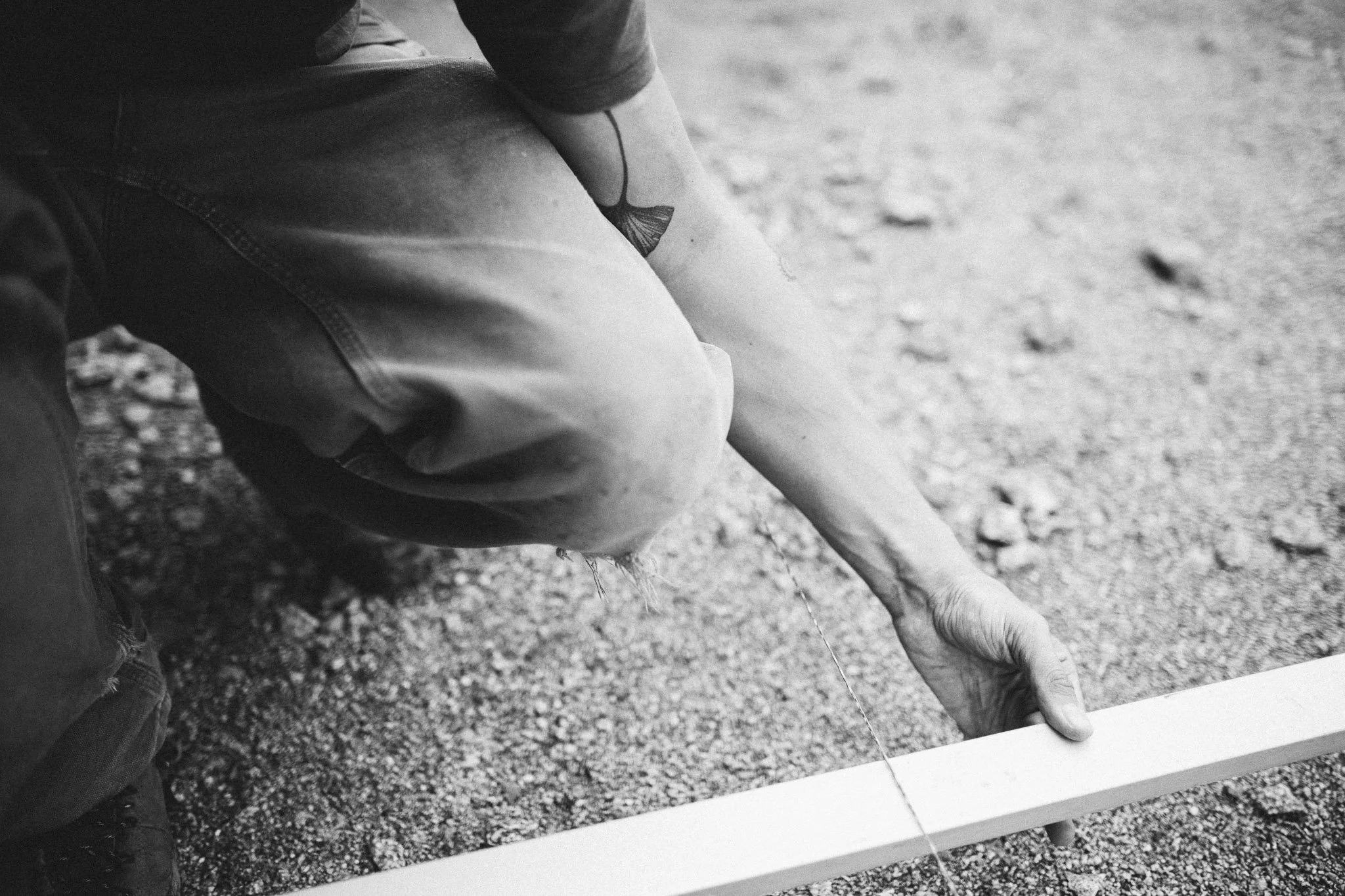 Nahaufnahme einer Person, die auf den Boden knien und eine weiße Holzlatte auf dem Boden positionieren