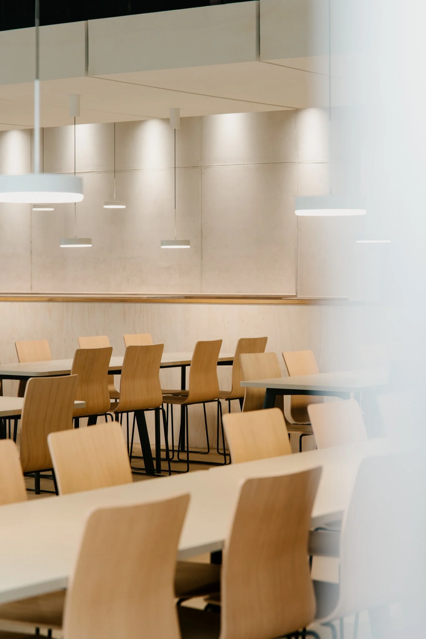 Leerer moderner Café- oder Restaurantraum mit Holzstühlen, weißen Tischen und weißen Lampen