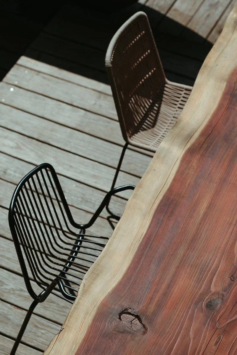 Zwei schwarze Küchenstühle auf einem Holzdeck neben einem Baumstamm