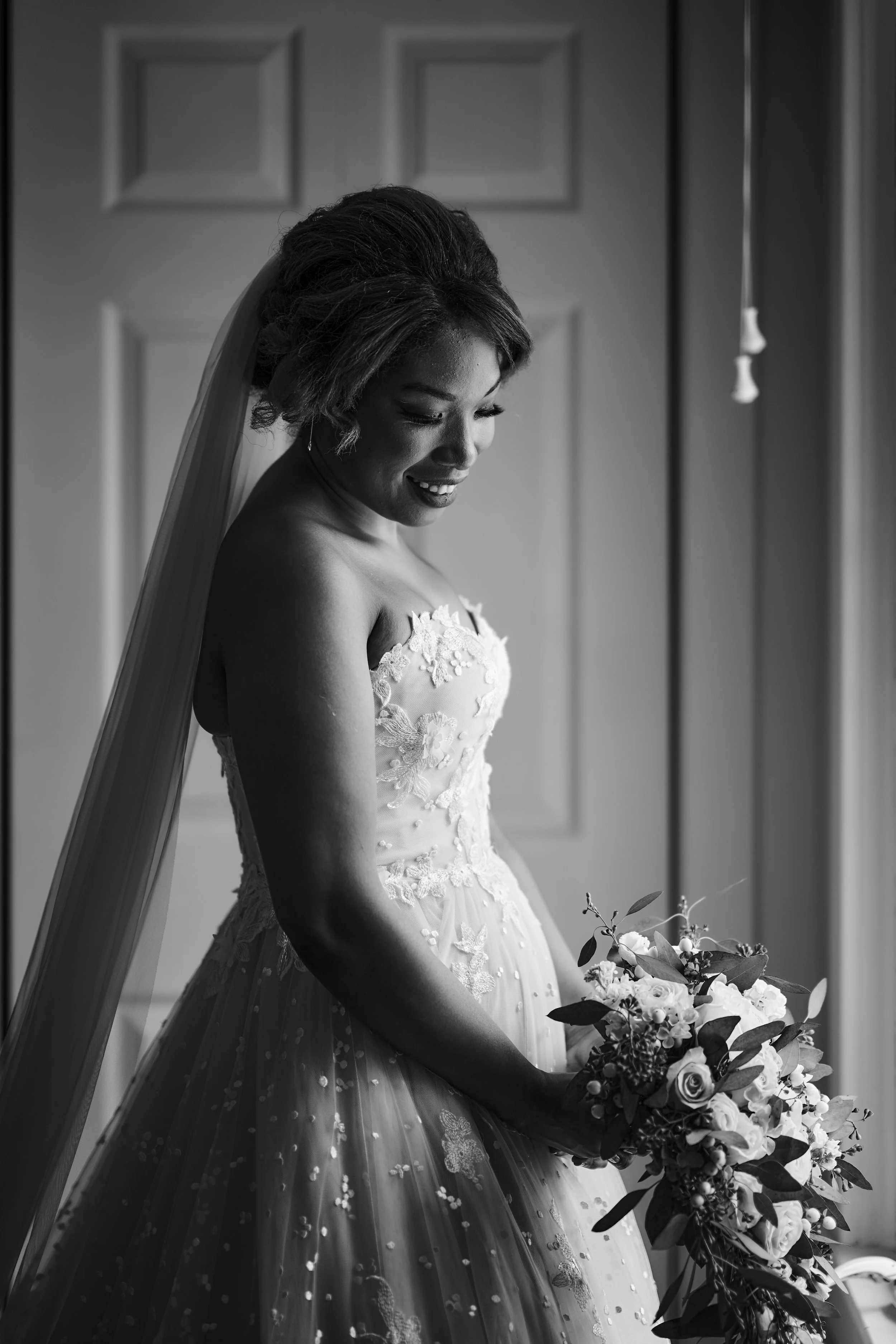 Black and white photo of a smiling bride in a wedding dress holding a bouquet of flowers.