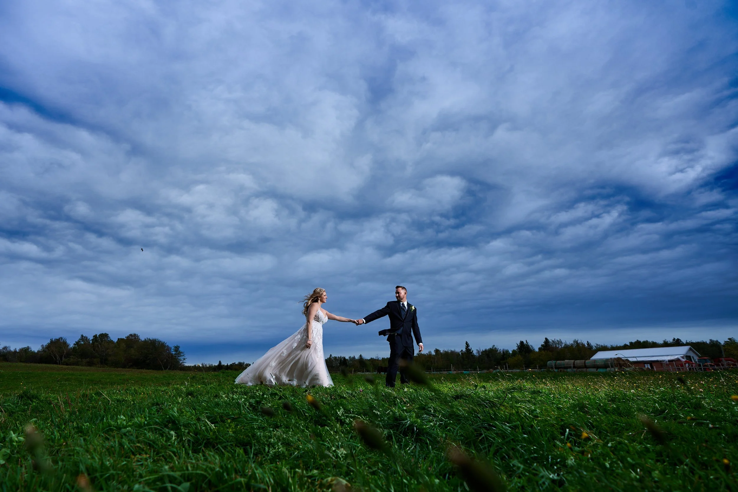 Bride and groom holding hands in a grassy field under a cloudy sky in the eye of a hurricane.