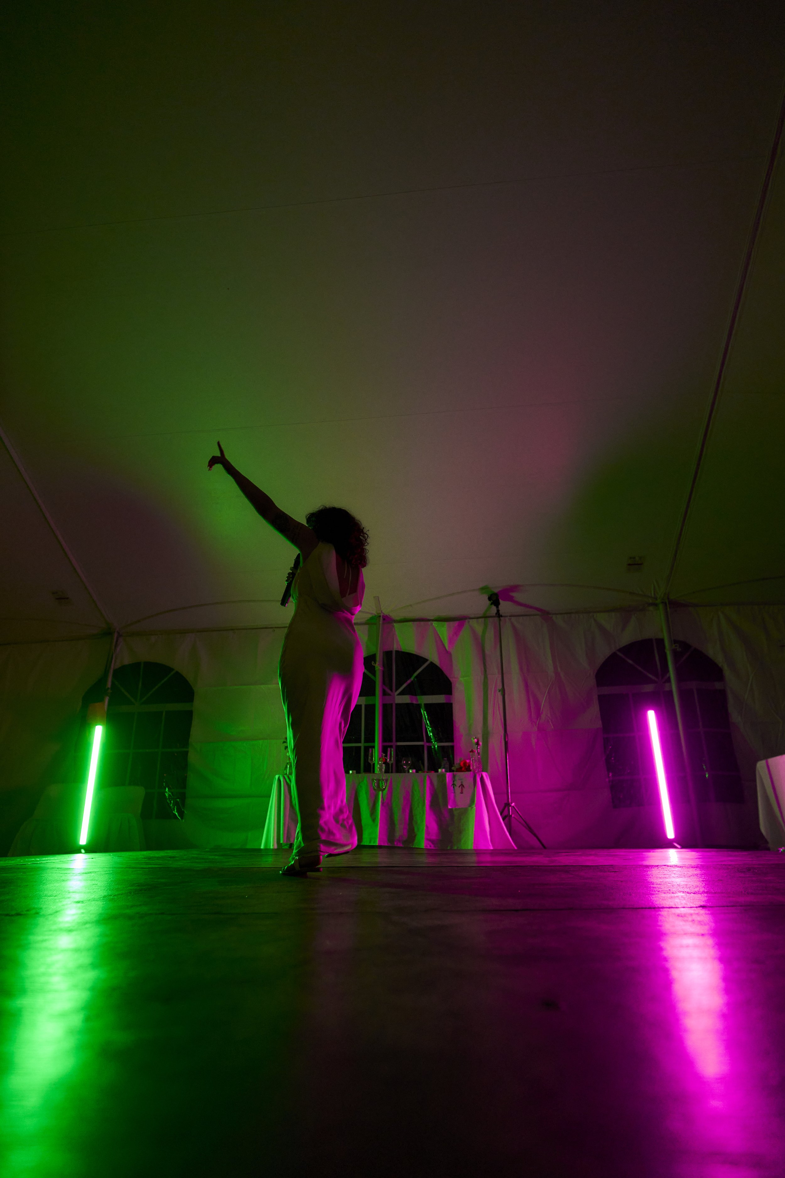 Woman dancing on a stage illuminated with colorful green and pink lights inside a large tent.