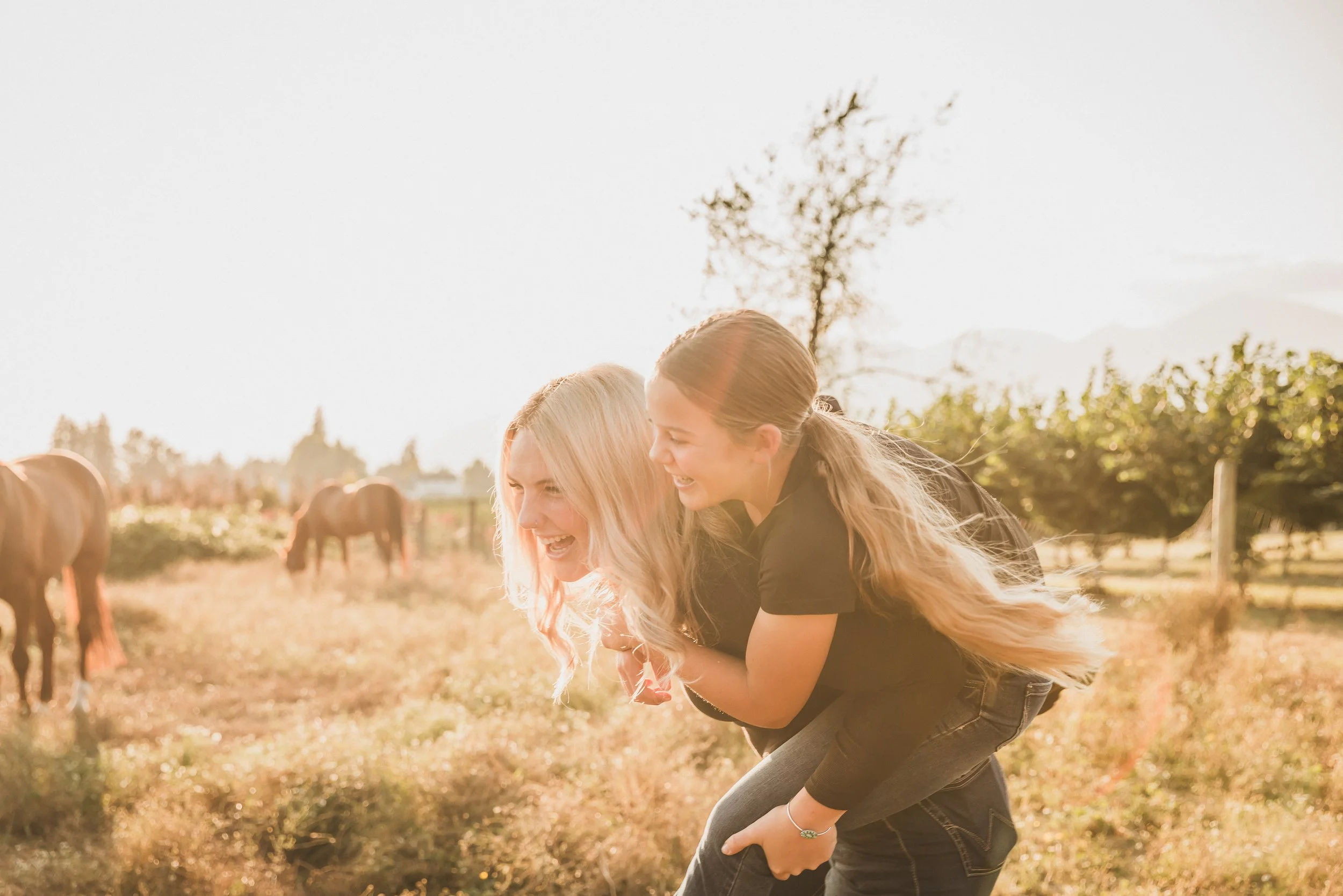 siblings 2 sisters playing in the field with their horses at golden hour on the farm