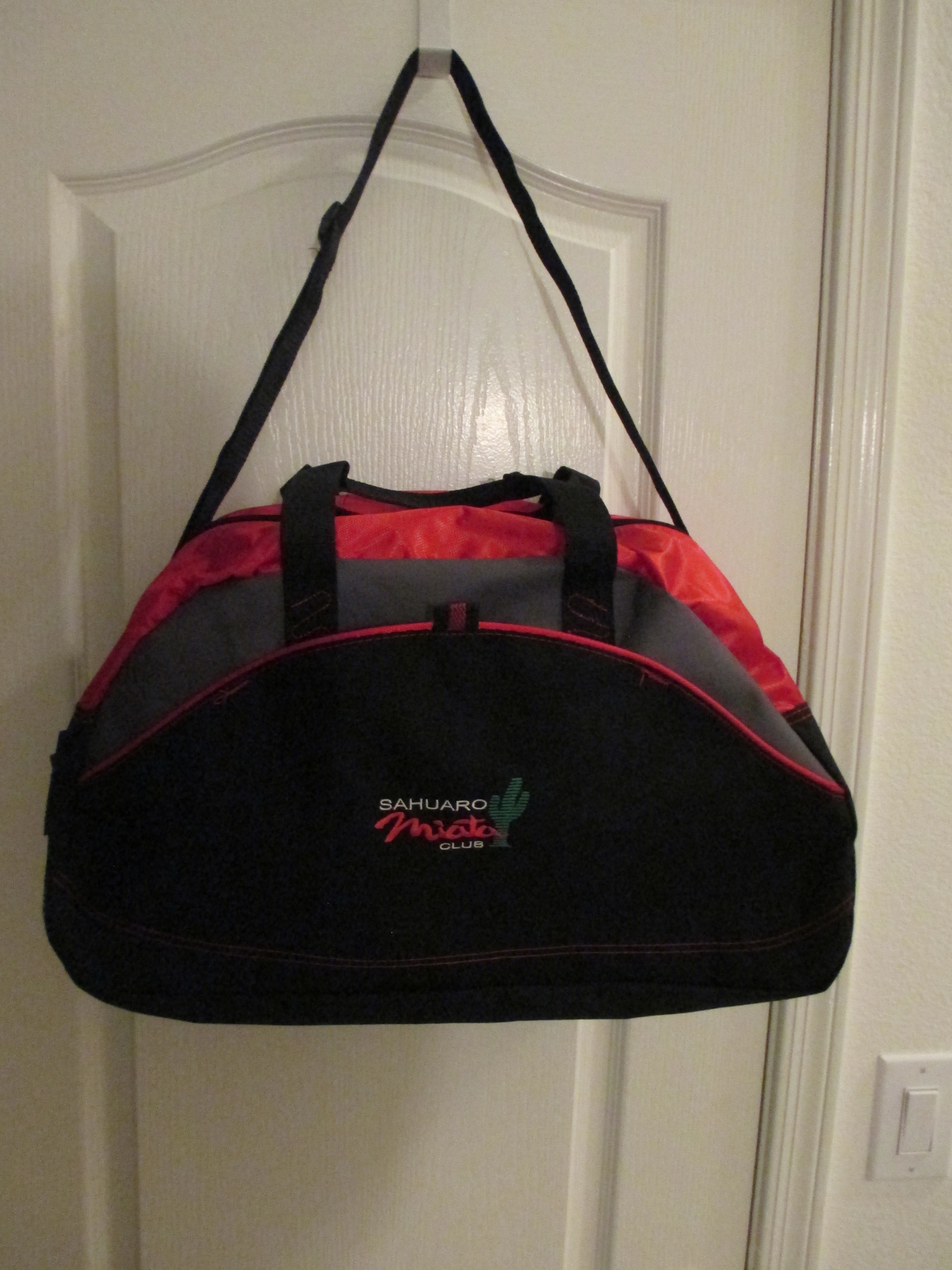 Port & Company tri-color domed top duffel bag Red/Grey/Black with red accent stitching and cording. Bag is soft sided and is 8 1/2 “ deep, 21” long and 13” tall. It has carry handles and an adjustable, but not removable, shoulder strap. There is a two way center zipper on top with an elastic top mesh outside pocket on one end. The front of the bag, where the Club logo is, has a pocket with three tuck access points. Now $18.00 - Special 2 for $34.00
