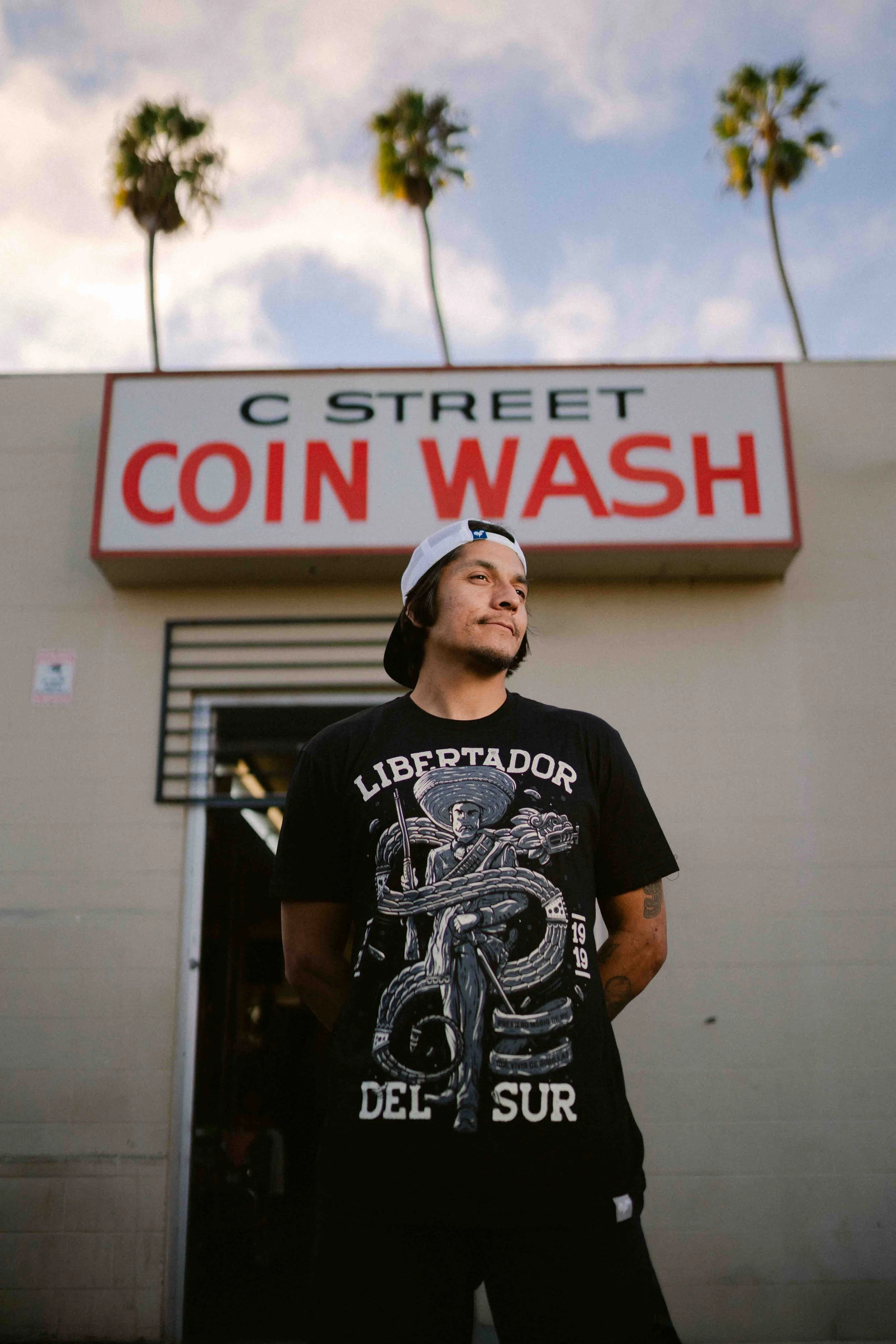 A man standing in front of a coin wash building with a sign that reads 'C Street Coin Wash' in Downtown Oxnard photographed by Humberto Rosales , 