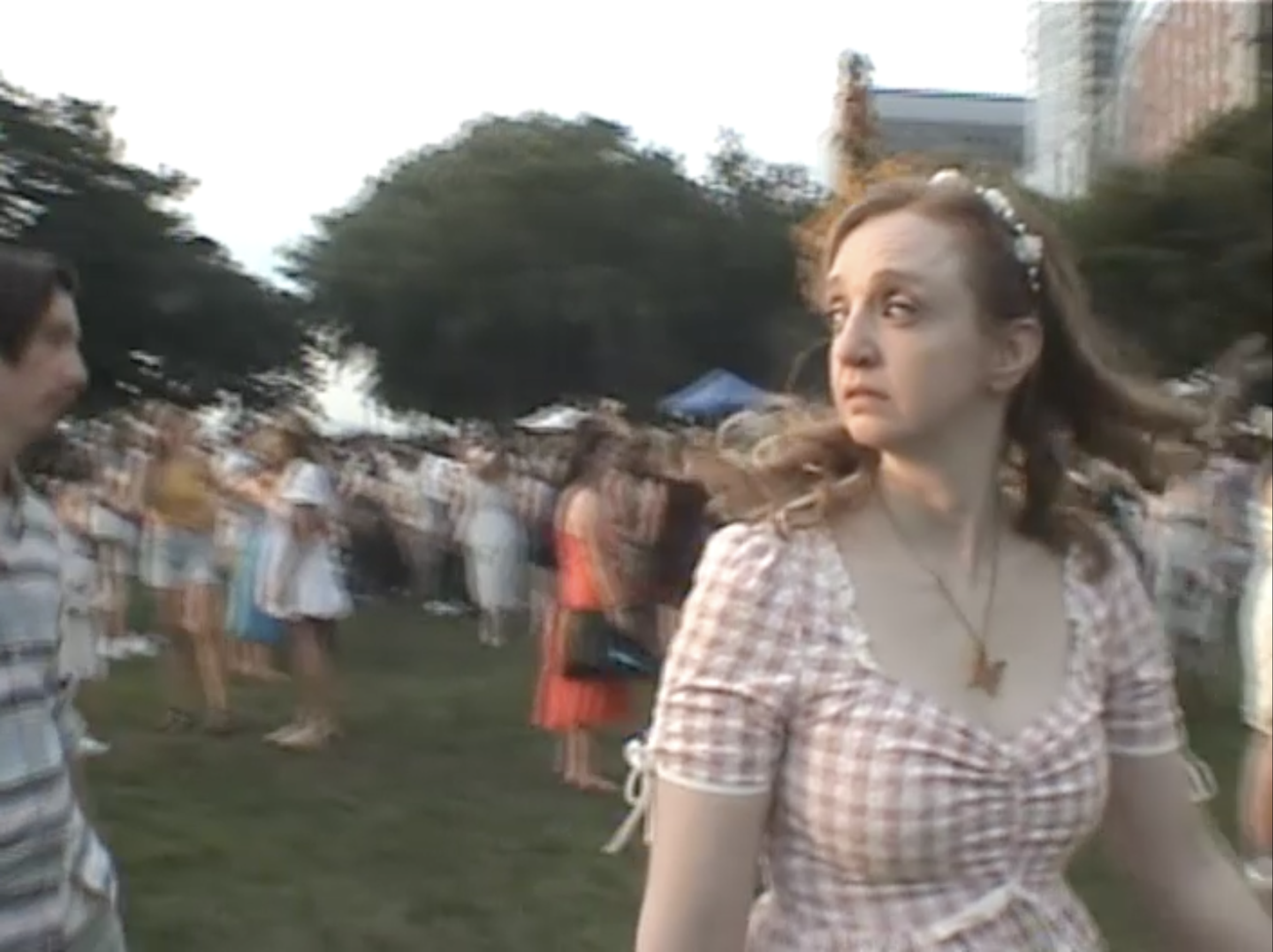 A young woman with curly hair and floral hair accessories wearing a plaid shirt at an outdoor event.