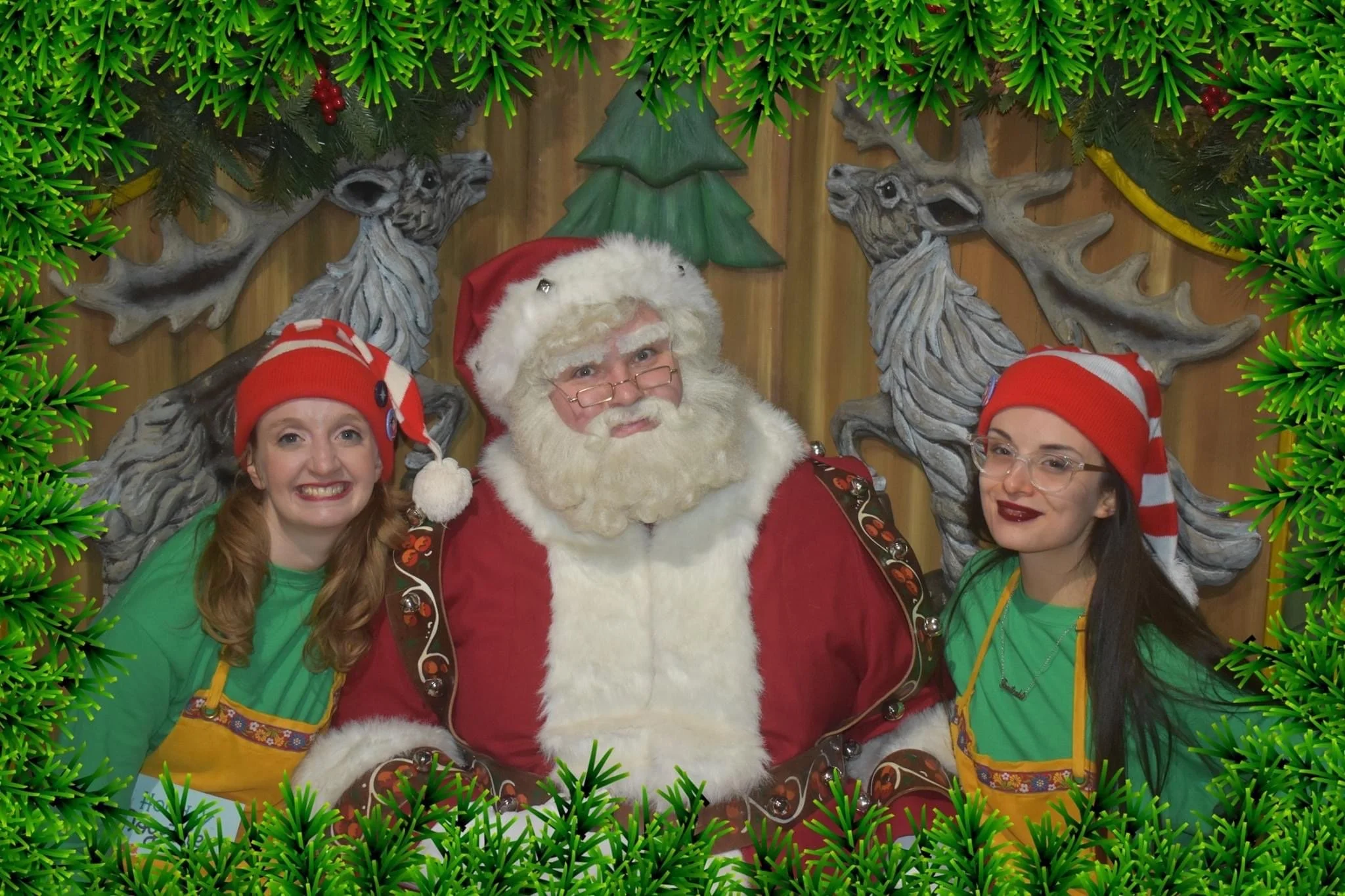 Three women and a man dressed as Santa Claus pose together in front of Christmas decorations, with a green garland border around the image.