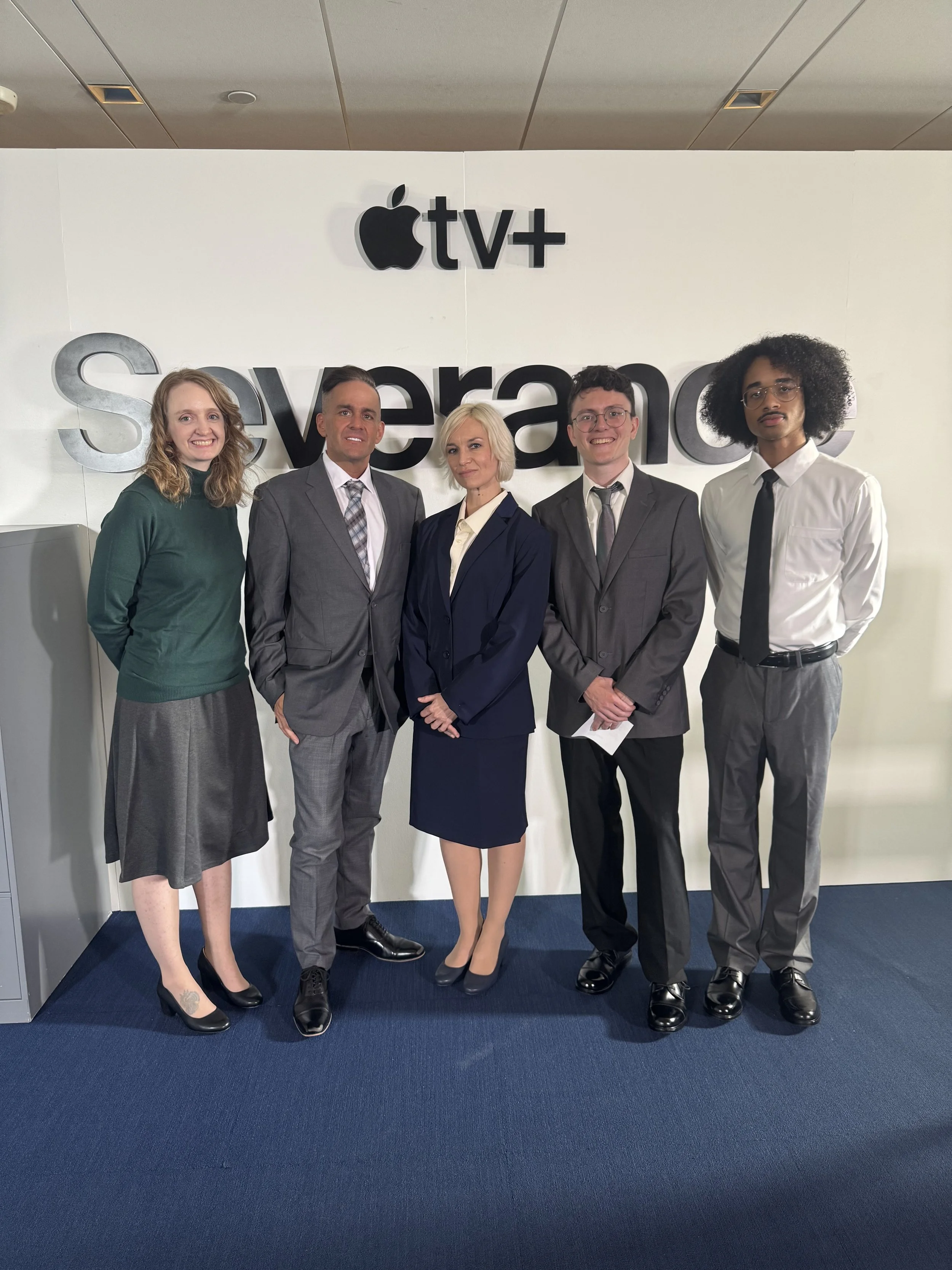 Group of five people dressed in formal business attire standing in front of a wall with the Apple logo and the words 'tv+' and 'Svovera'.