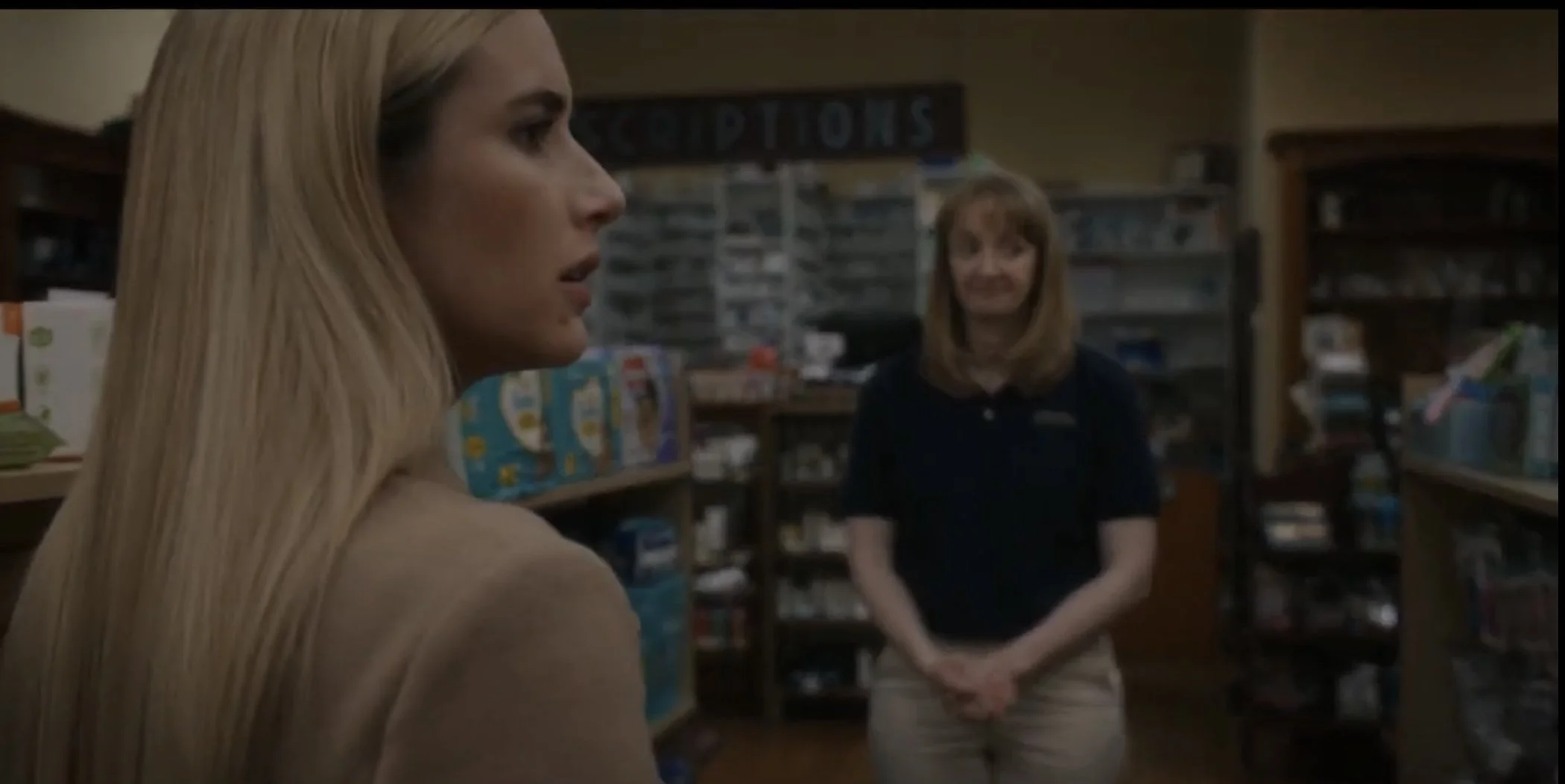 A woman with long blonde hair in a grocery store aisle, facing to the left, with another woman with shoulder-length hair standing behind her, smiling.