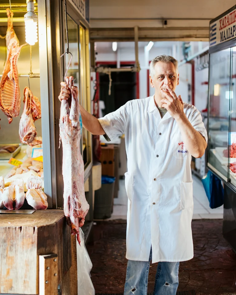 A local butcher has a smoke while hanging onto a skinned lamb.