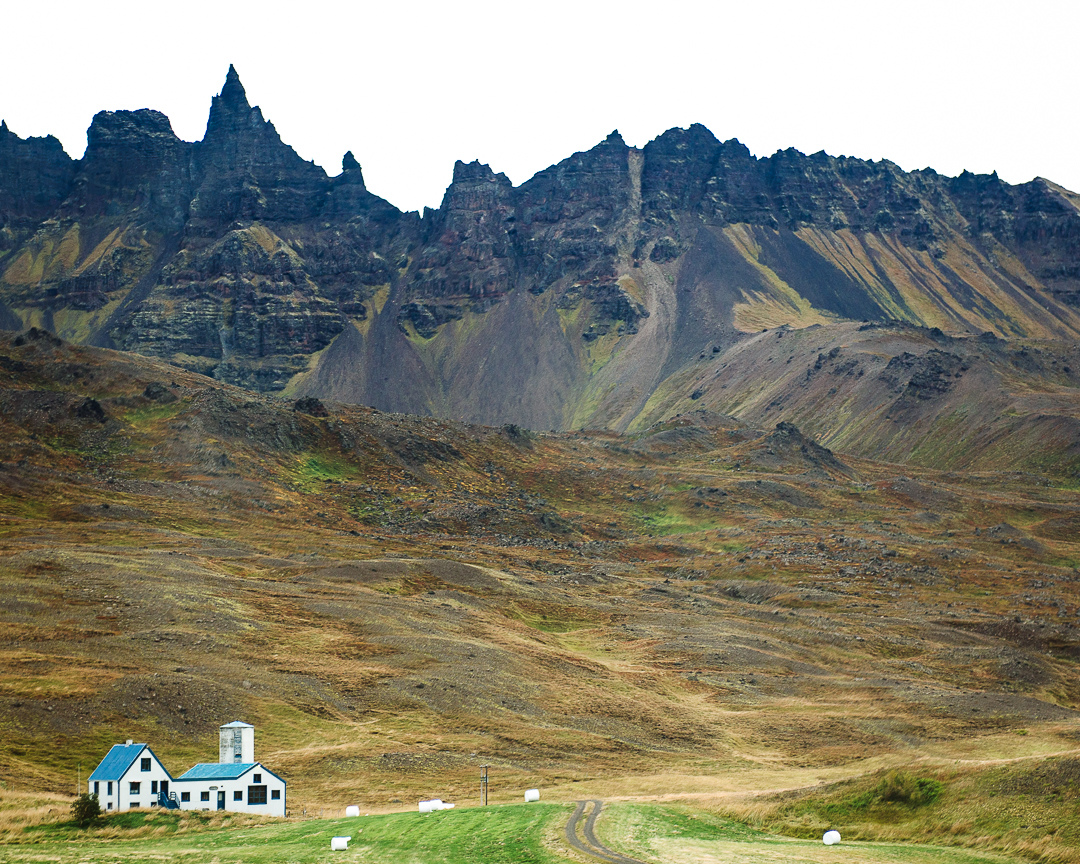 Farmhouse sits below a rugged mountain range.