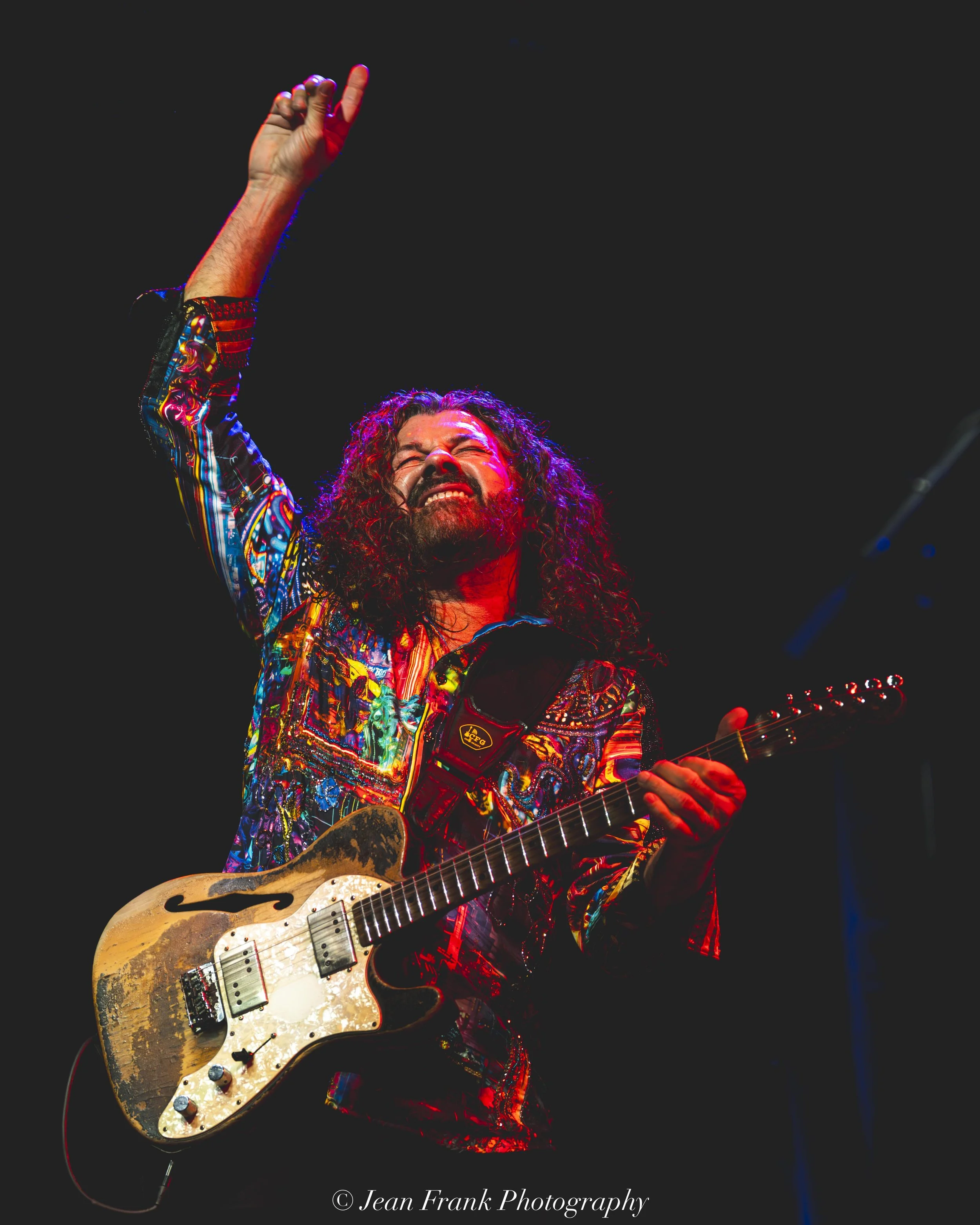 Tab Benoit holds well-worn electric guitar while pointing up, with closed eyes